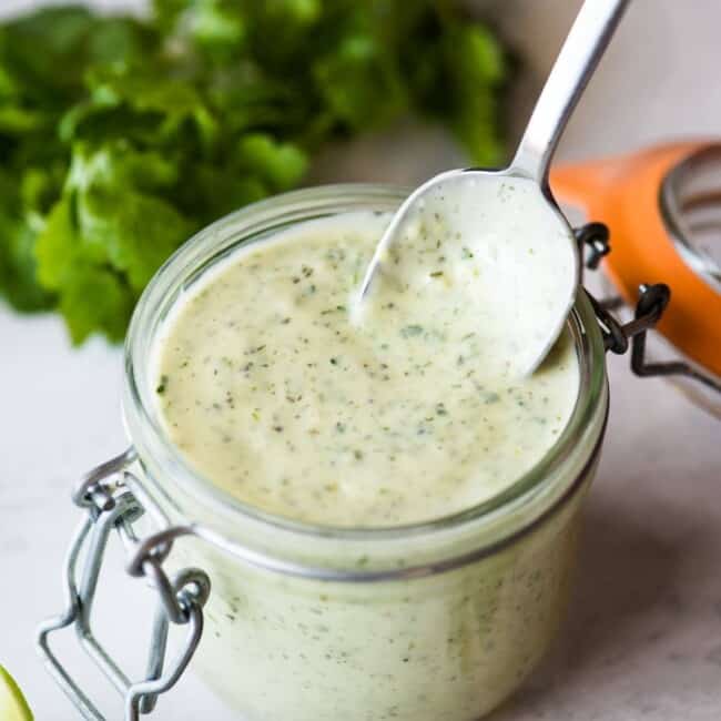 A spoon stirring jalapeno ranch in a jar.
