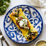 A Mexican omelet on a plate topped with chunky salsa and sour cream.