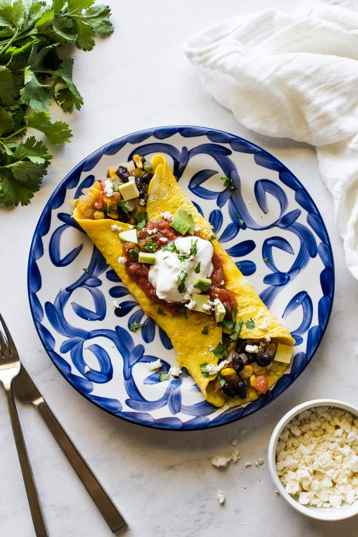 A Mexican omelet on a plate topped with chunky salsa and sour cream.
