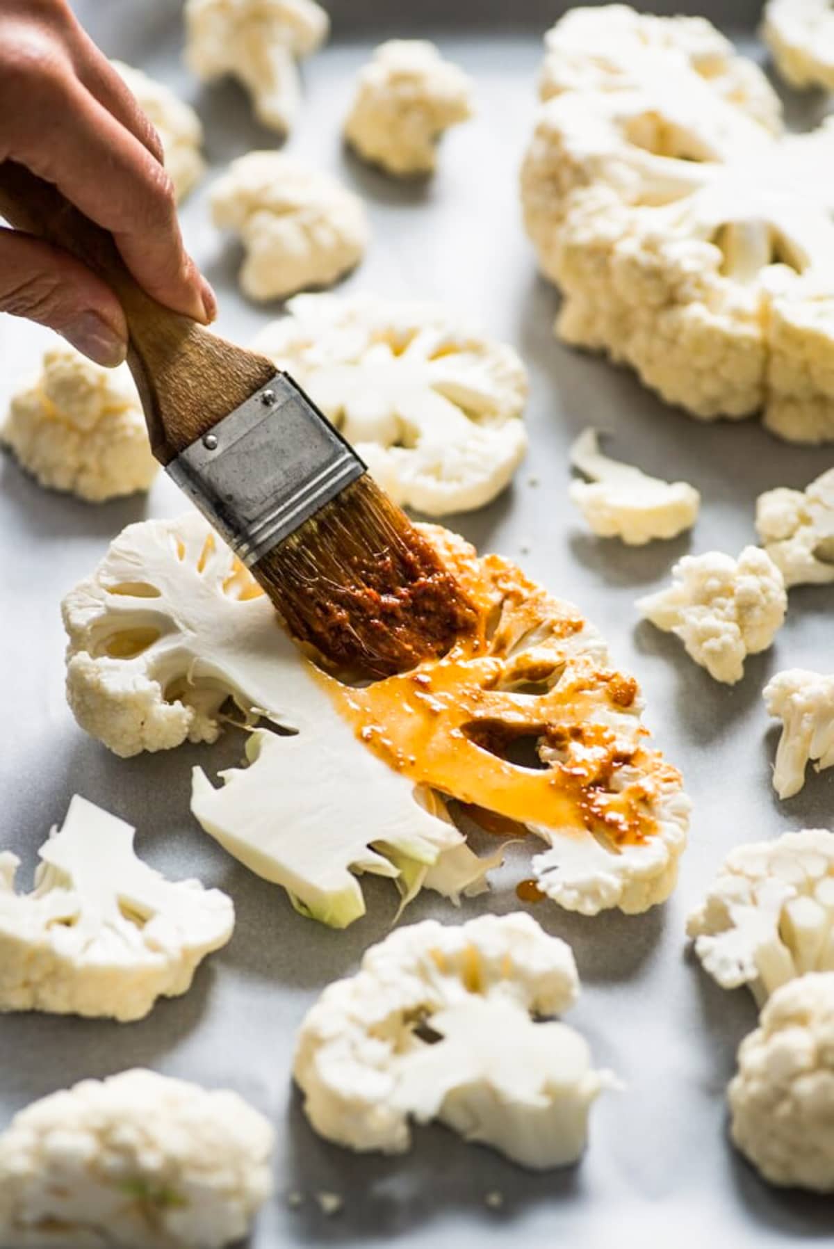 A hand brushing on a chipotle sauce onto cauliflower slices.