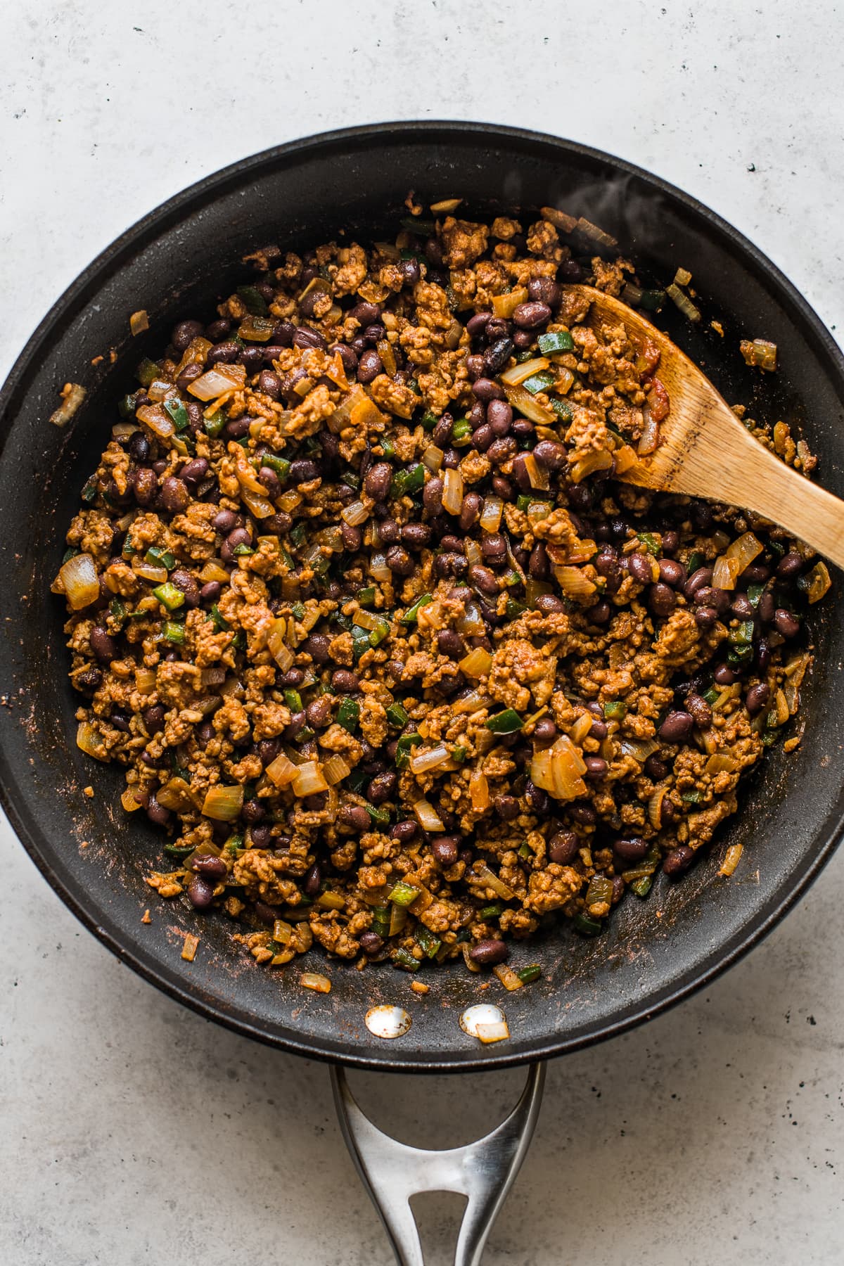 Cooked filling made from ground chicken, black beans, peppers in a skillet.