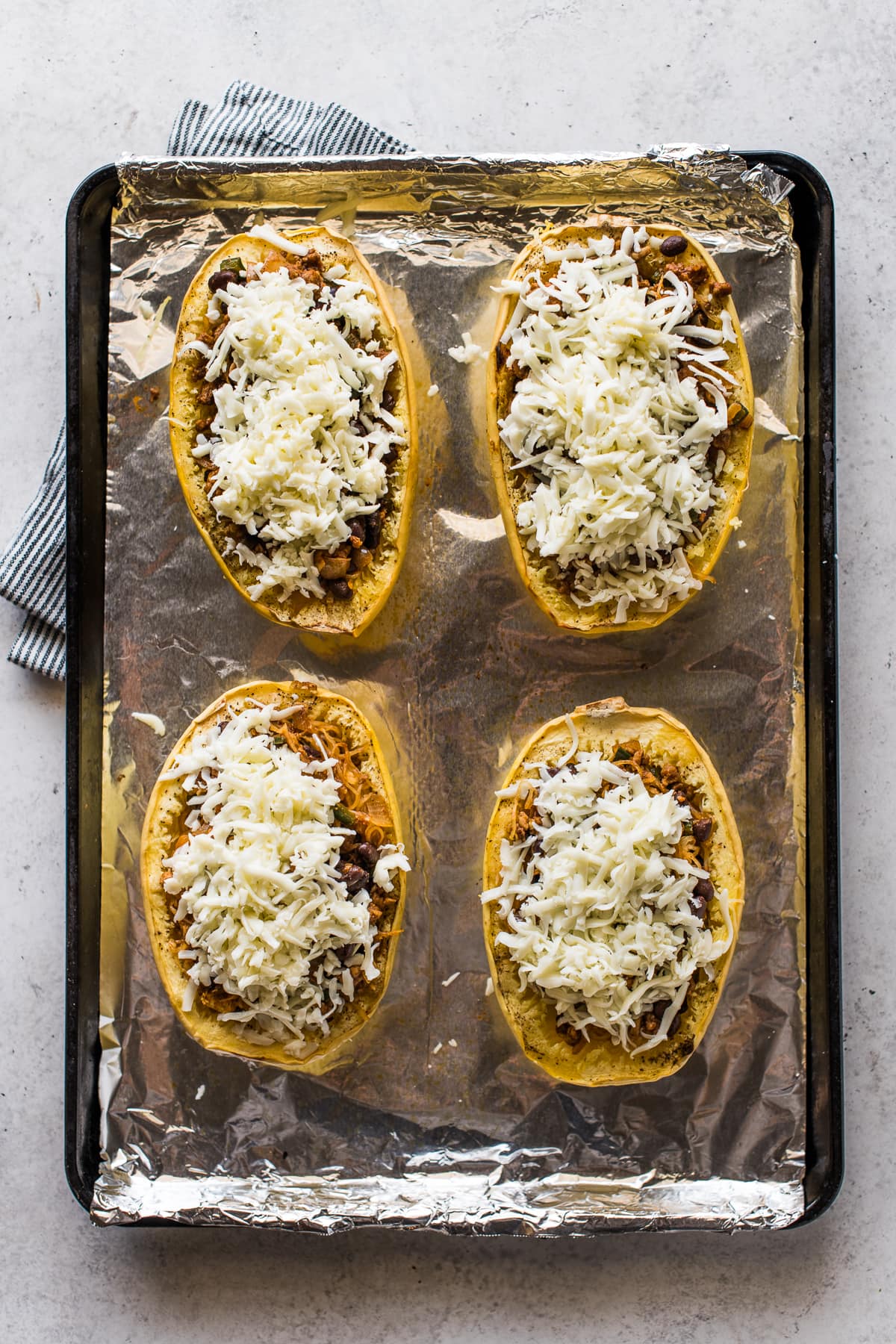 Stuffed spaghetti squash topped with shredded cheese on a baking sheet.