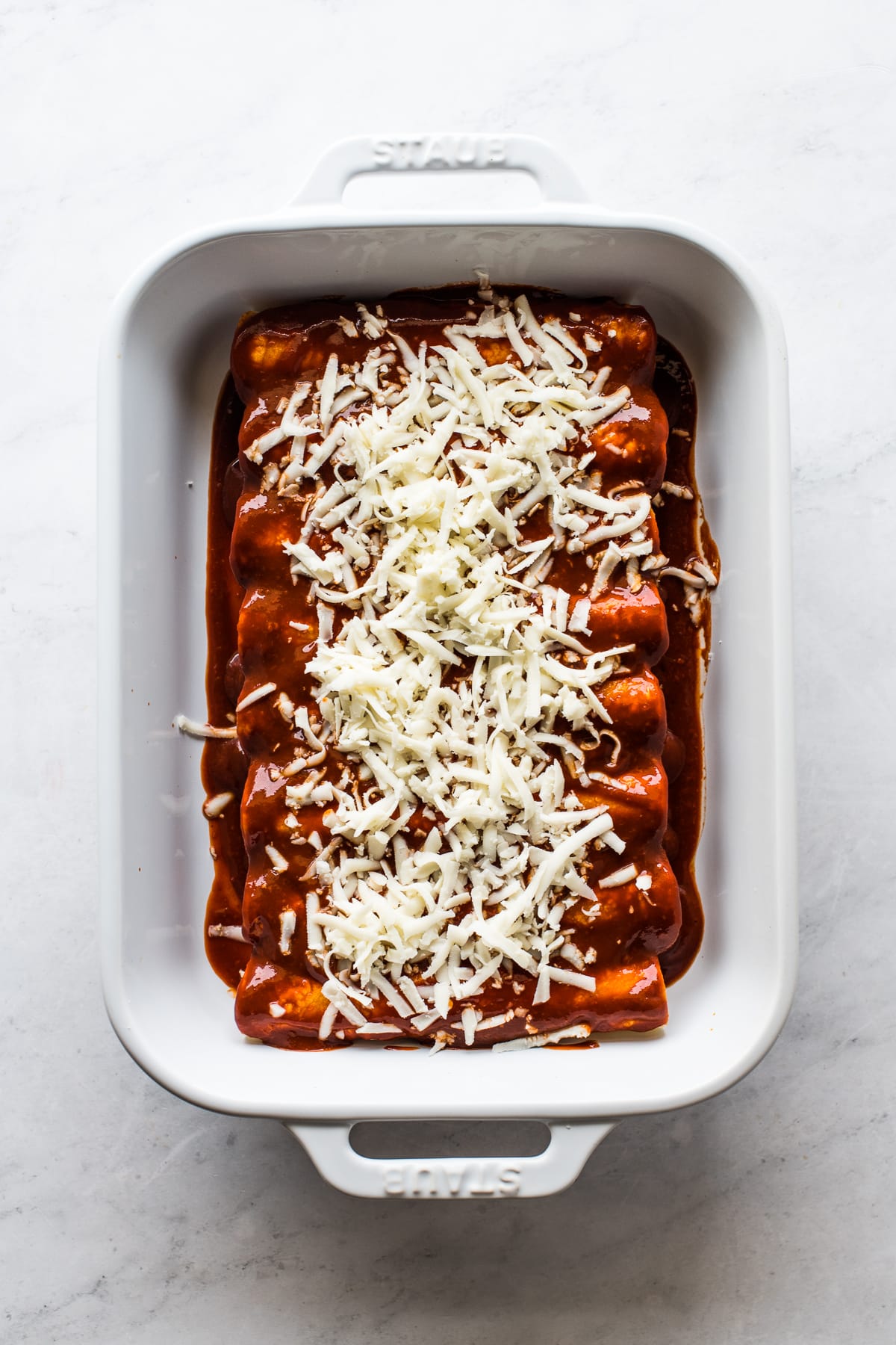 A baking dish with cheese enchiladas topped with more shredded cheese.