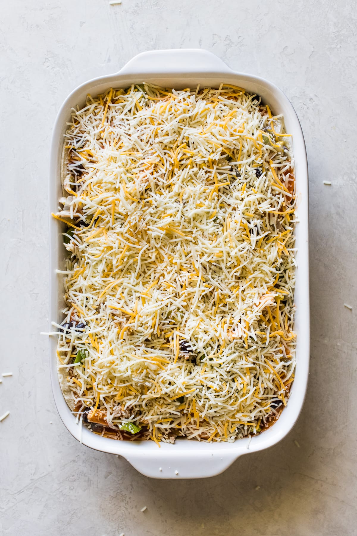 Shredded cheese on top of chicken enchilada casserole before baking.