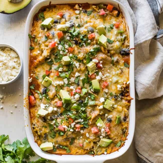 Chicken enchilada casserole topped with cilantro, diced tomatoes, and avocados.