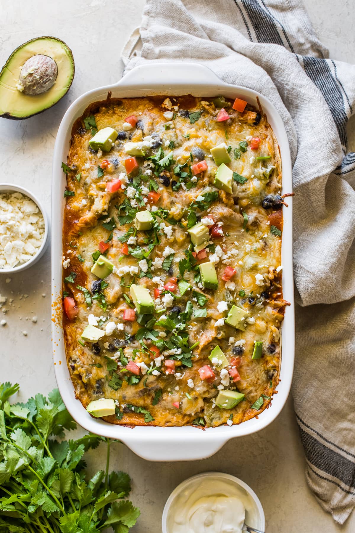 Chicken enchilada casserole topped with cilantro, diced tomatoes, and avocados.