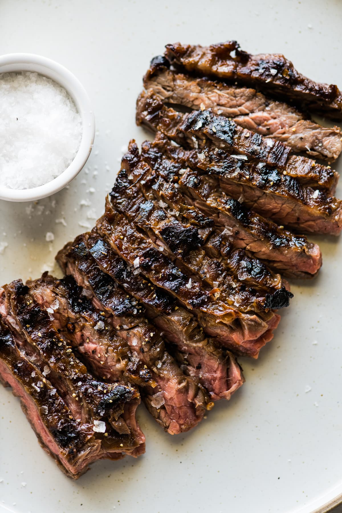 Sliced grilled skirt steak sprinkled with flaky sea salt on a white plate.