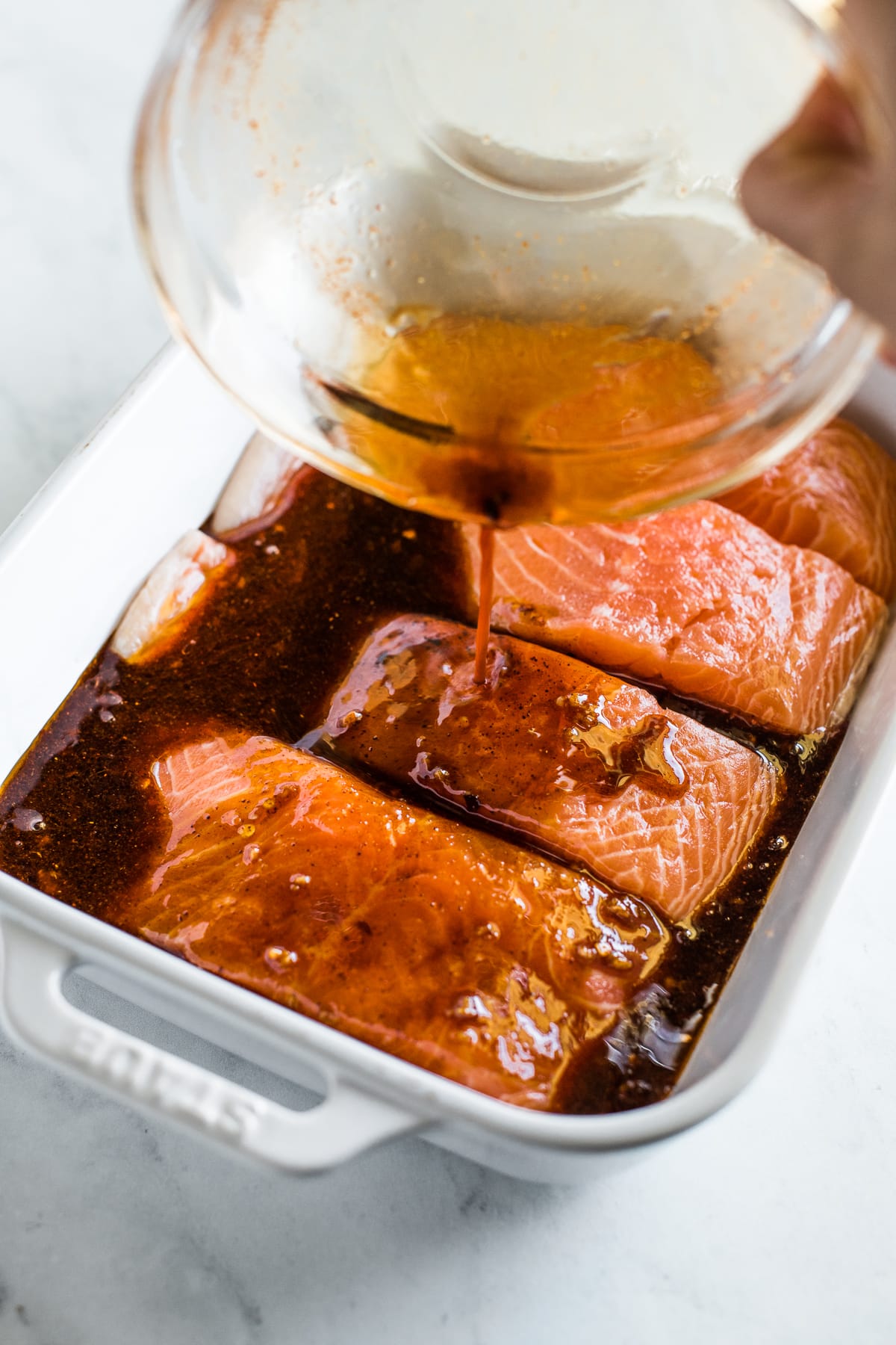 Chili garlic marinade being poured on salmon filets.
