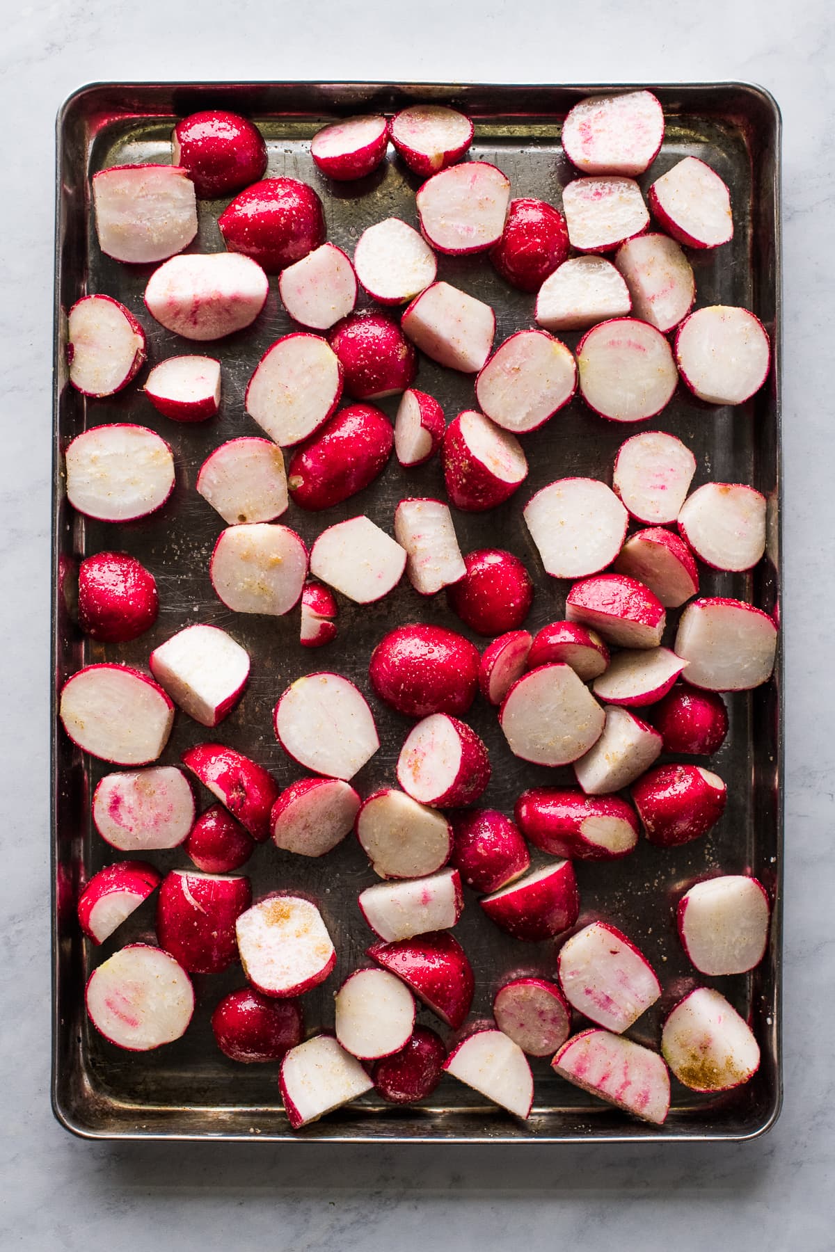 Radishes tossed with olive oil and spices on a sheet pan.