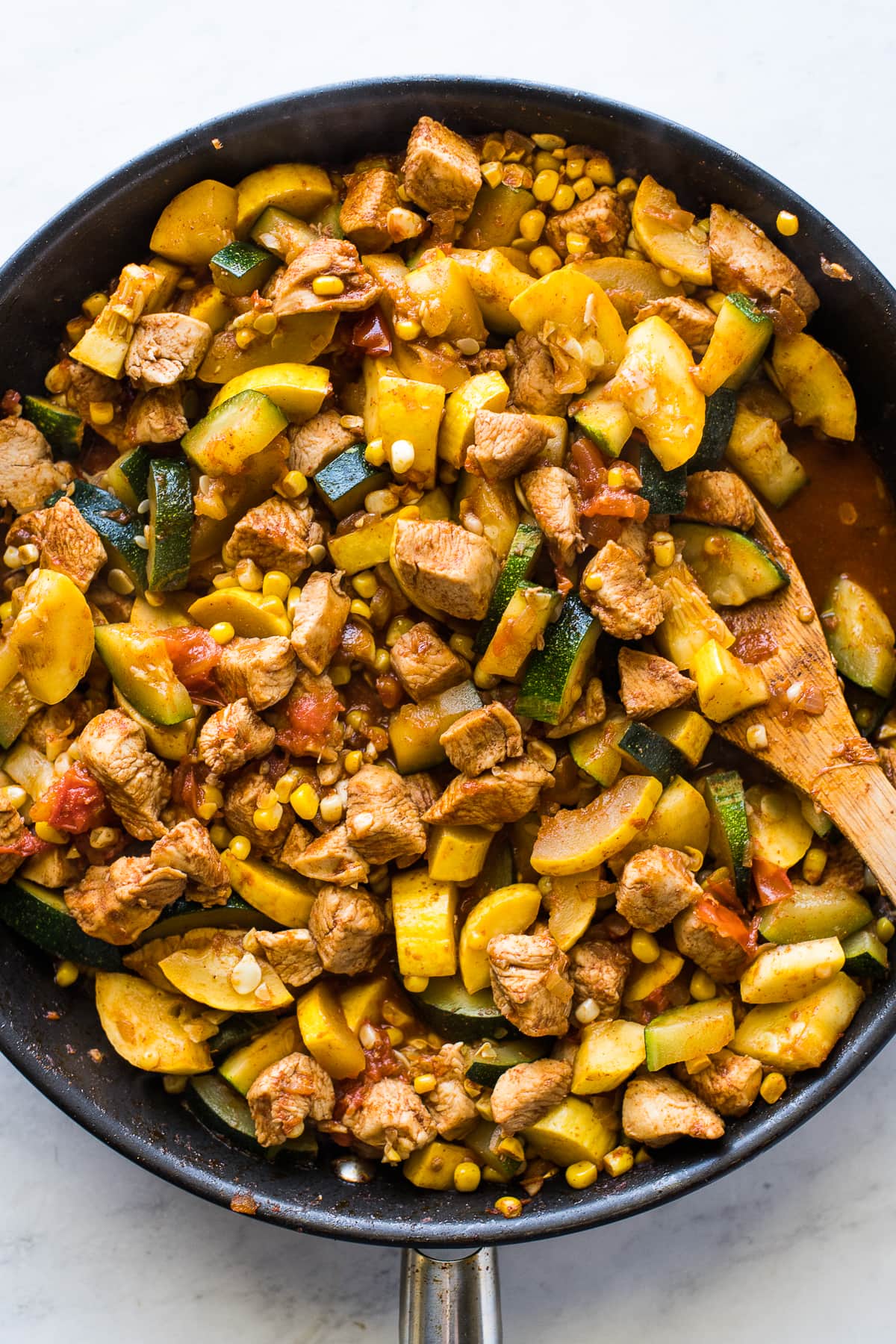 Cooking chicken and squash in a skillet with a wooden spoon.