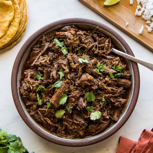 Shredded Instant Pot barbacoa in a large serving bowl garnished with fresh cilantro.