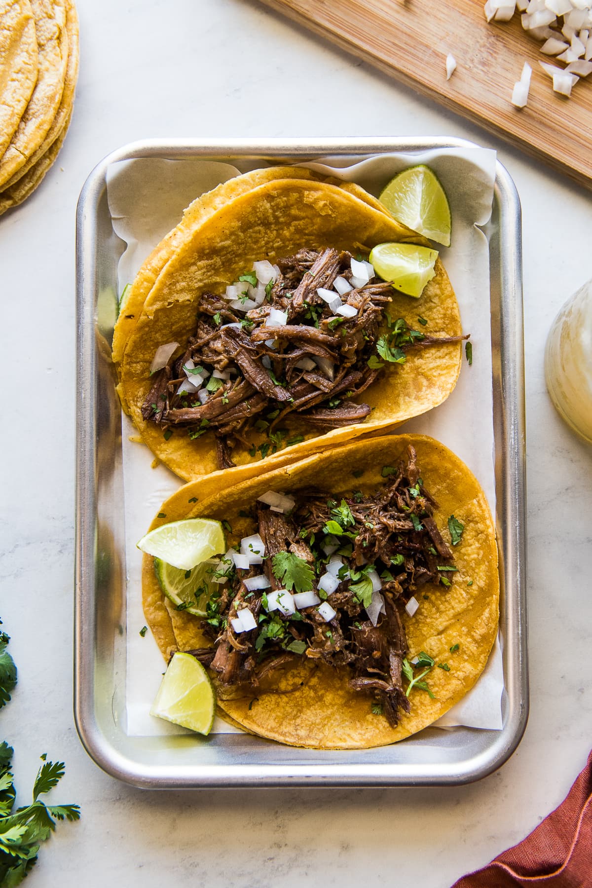 Instant Pot Barbacoa tacos topped with onions, cilantro, and lime wedges.