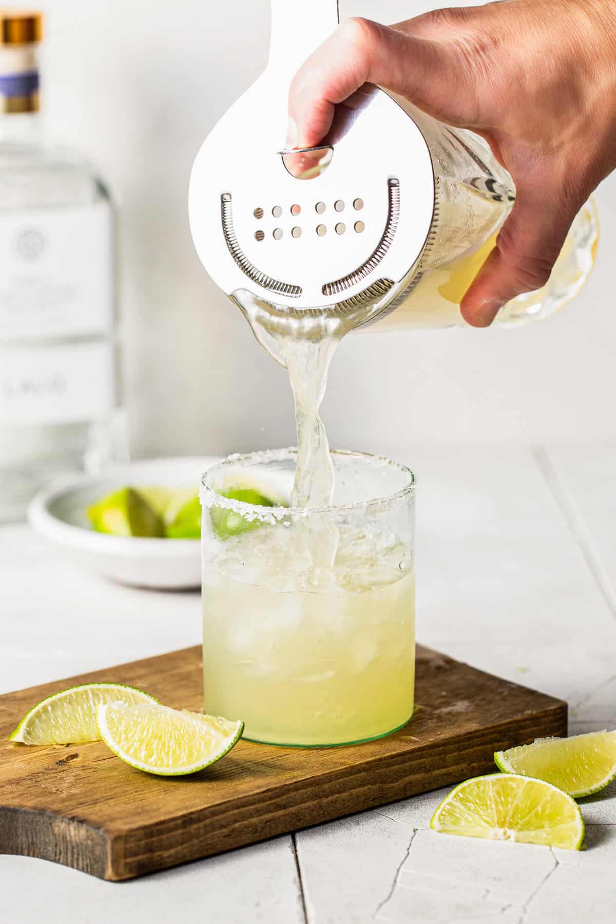 Pouring a classic margarita recipe from a cocktail shaker into a salted rim glass with ice