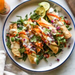 Air fryer chicken taquitos on a plate with lettuce and topped with sour cream, cilantro, salsa, and diced onions.