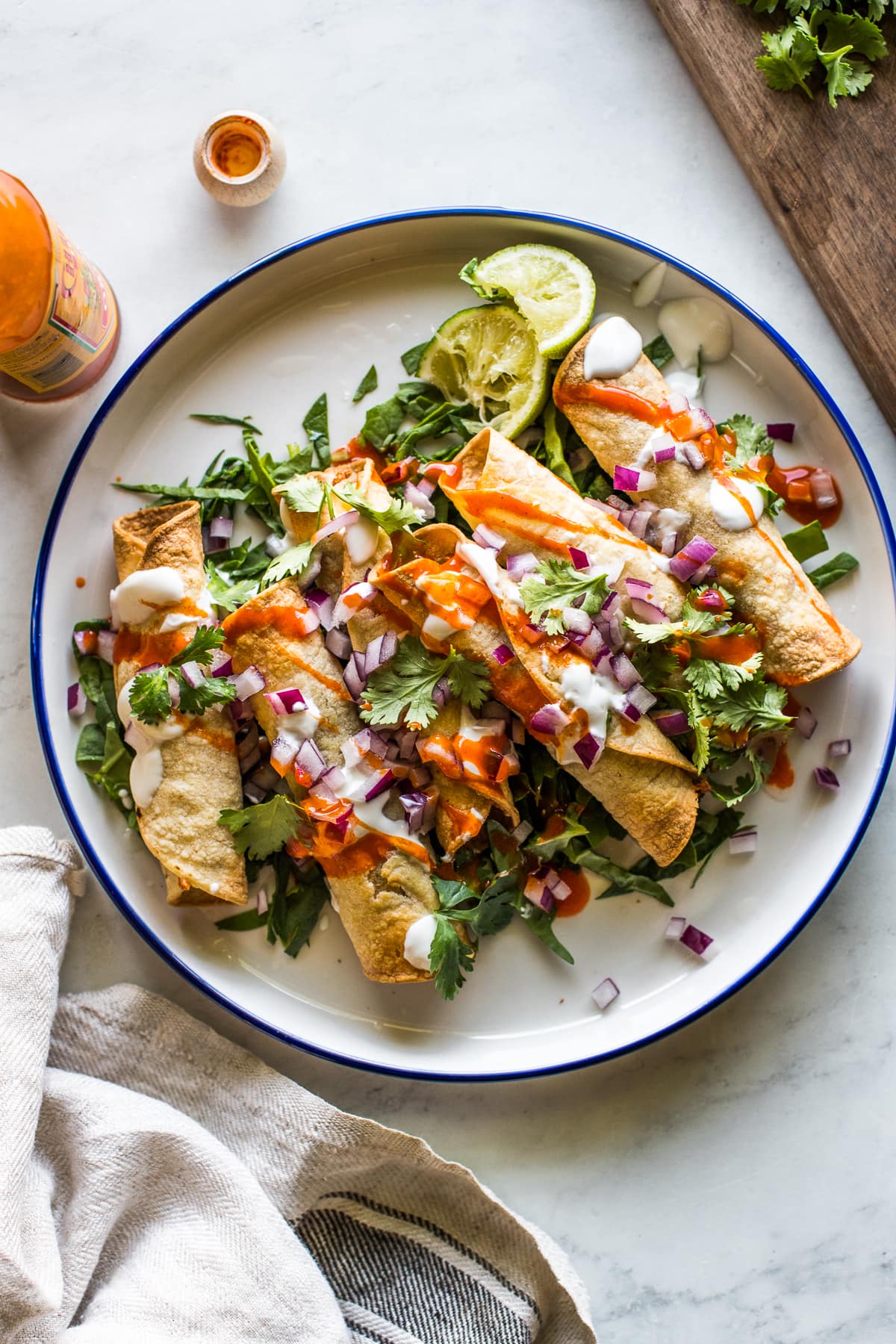 Air fryer chicken taquitos on a plate with lettuce and topped with sour cream, cilantro, salsa, and diced onions.