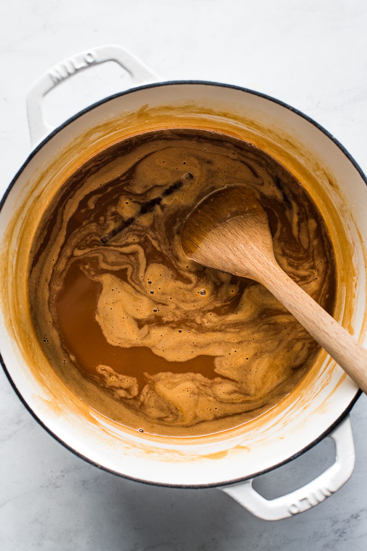 A wooden spoon stirring cajeta in a dutch oven.