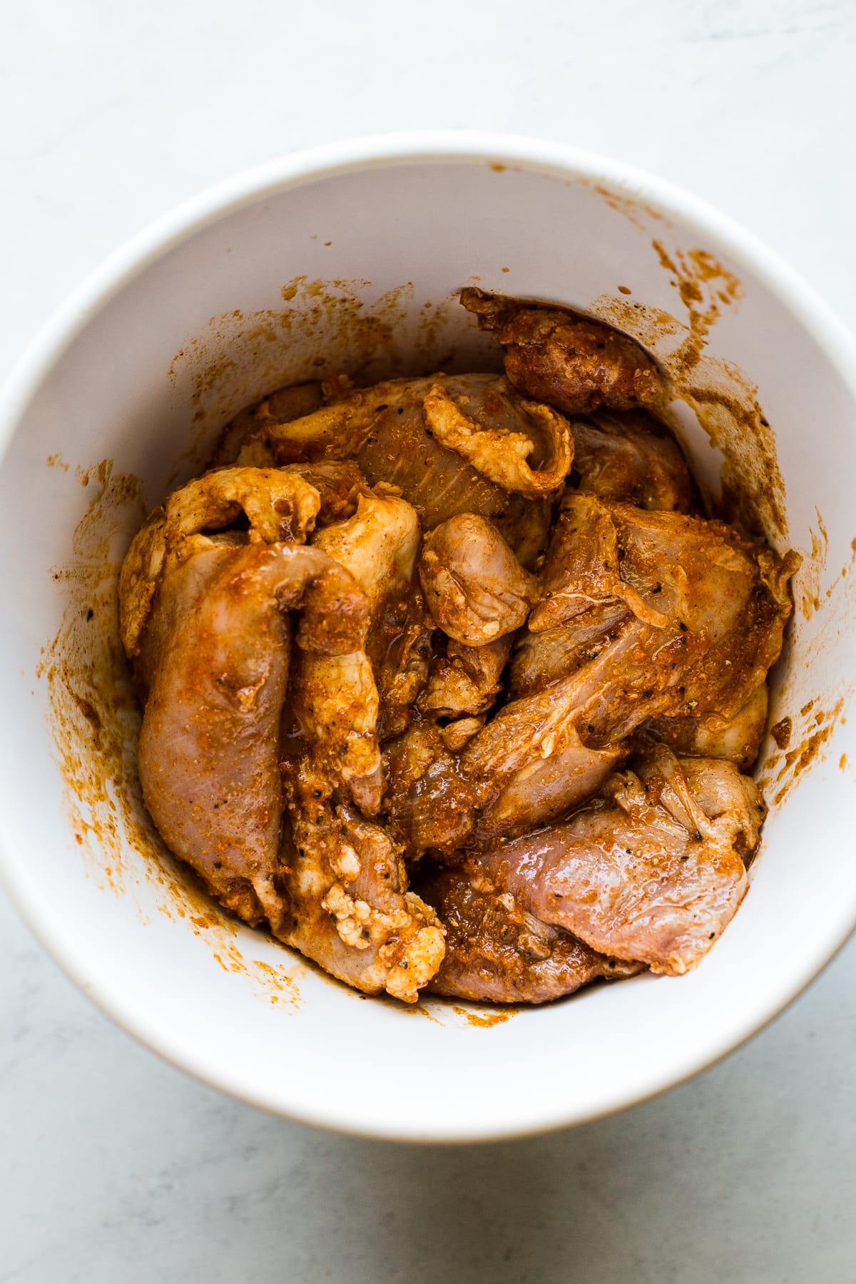 Boneless skinless chicken thighs in a bowl marinating in spices and lime juice.