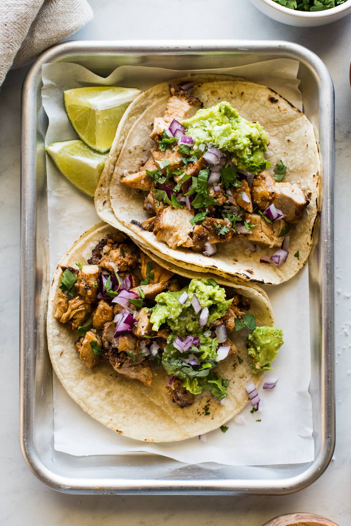 Easy Chicken Tacos topped with chopped cilantro, diced onions, smashed avocado, and lime wedges.