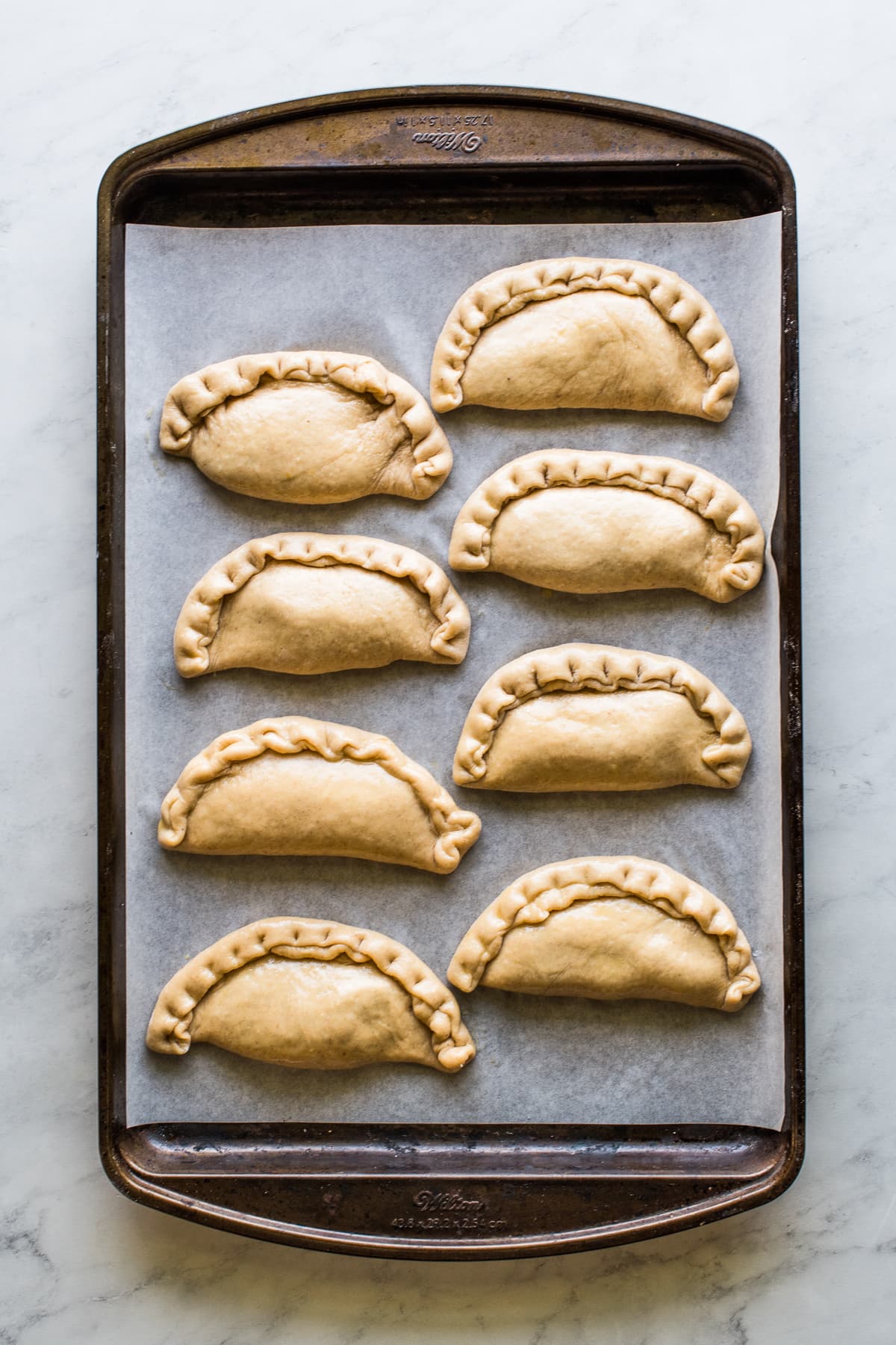 Sealed pumpkin empanadas on a baking sheet ready to be baked.