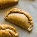 Pumpkin empanadas on a baking tray lined with parchment paper.