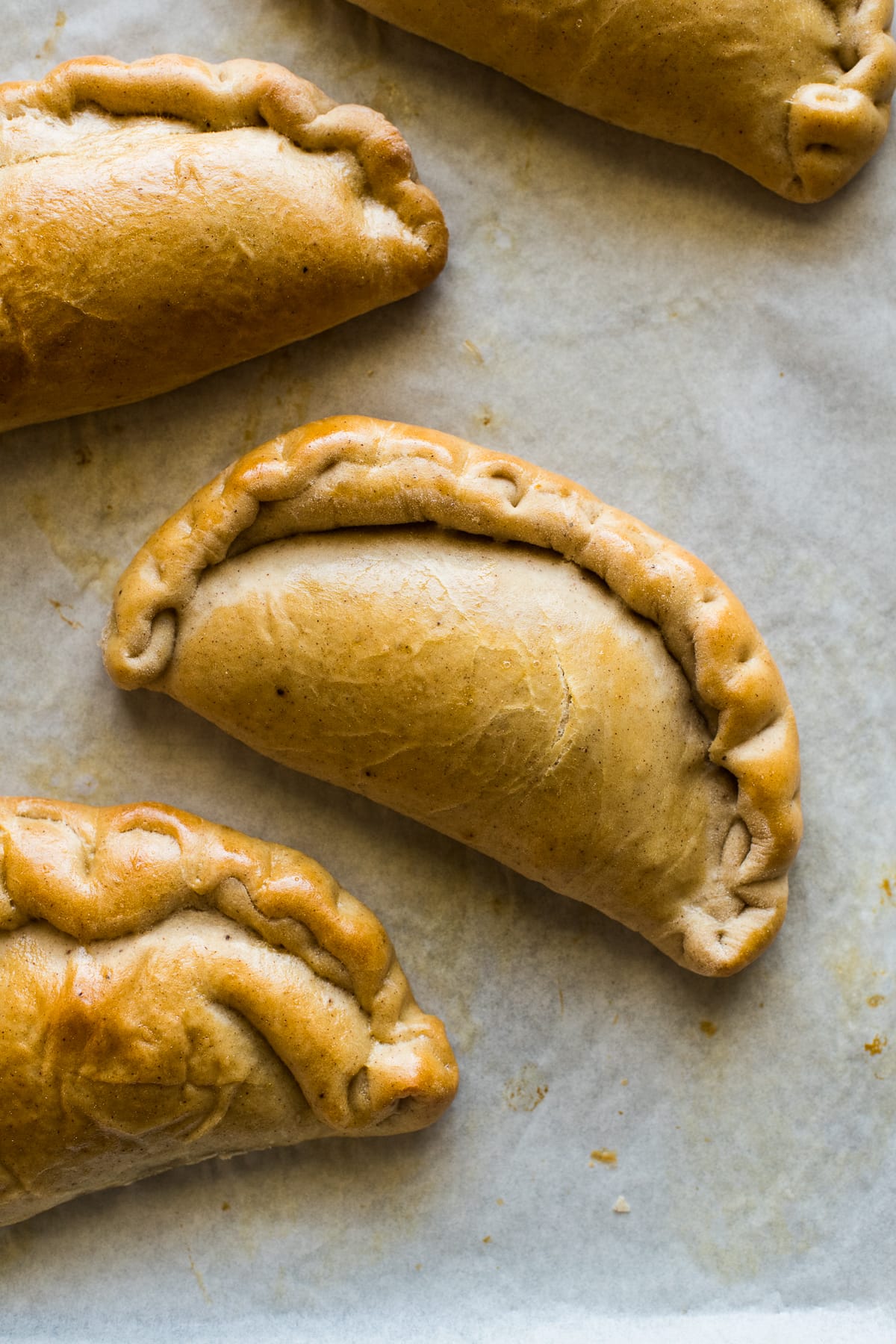 Pumpkin empanadas on a baking tray lined with parchment paper.