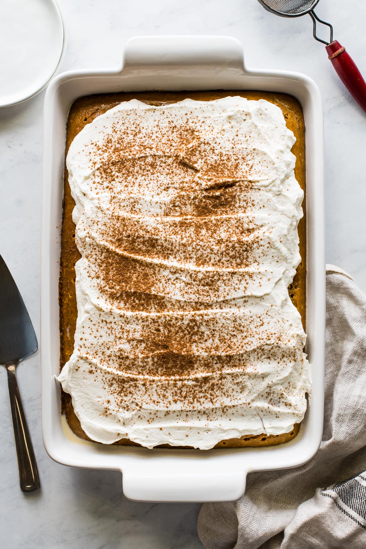 Pumpkin Tres Leches Cake in a baking pan topped with whipped cream and pumpkin spice seasoning.
