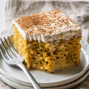 A slice of pumpkin tres leches cake topped with whipped cream and garnished with a dusting of pumpkin spice seasoning.