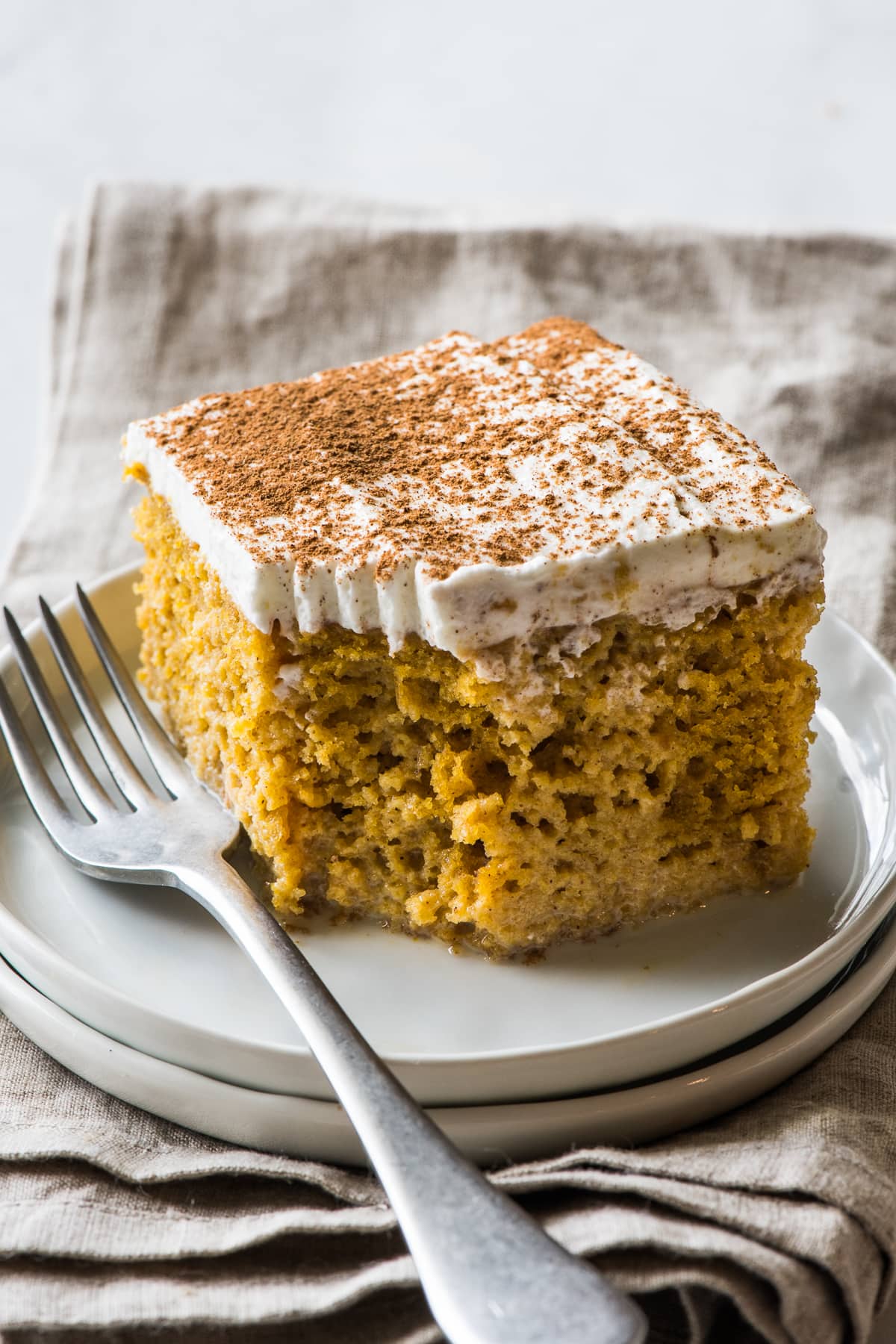 A slice of pumpkin tres leches cake topped with whipped cream and garnished with a dusting of pumpkin spice seasoning.