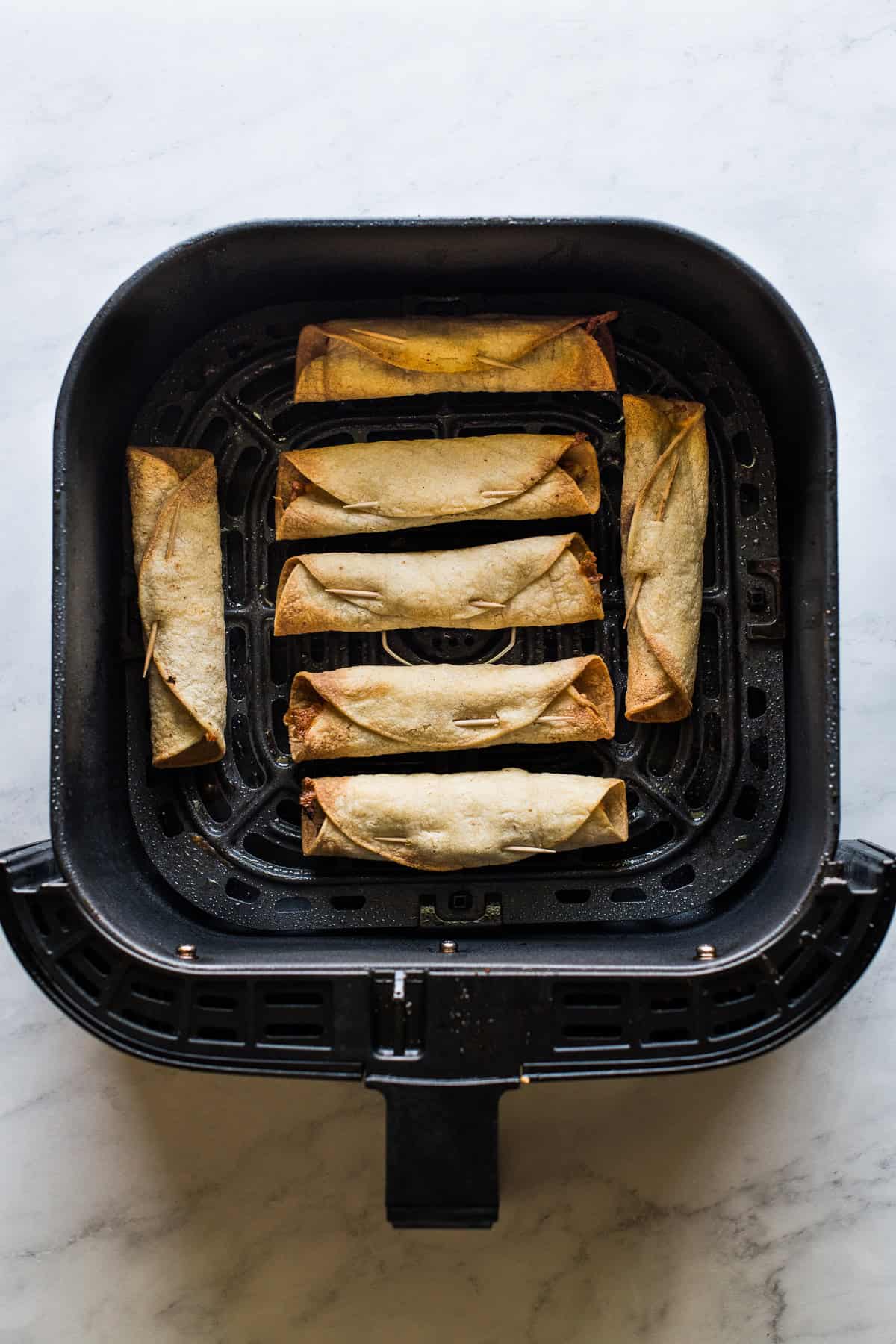 Crispy golden air fryer taquitos in the air fryer basket after cooking.