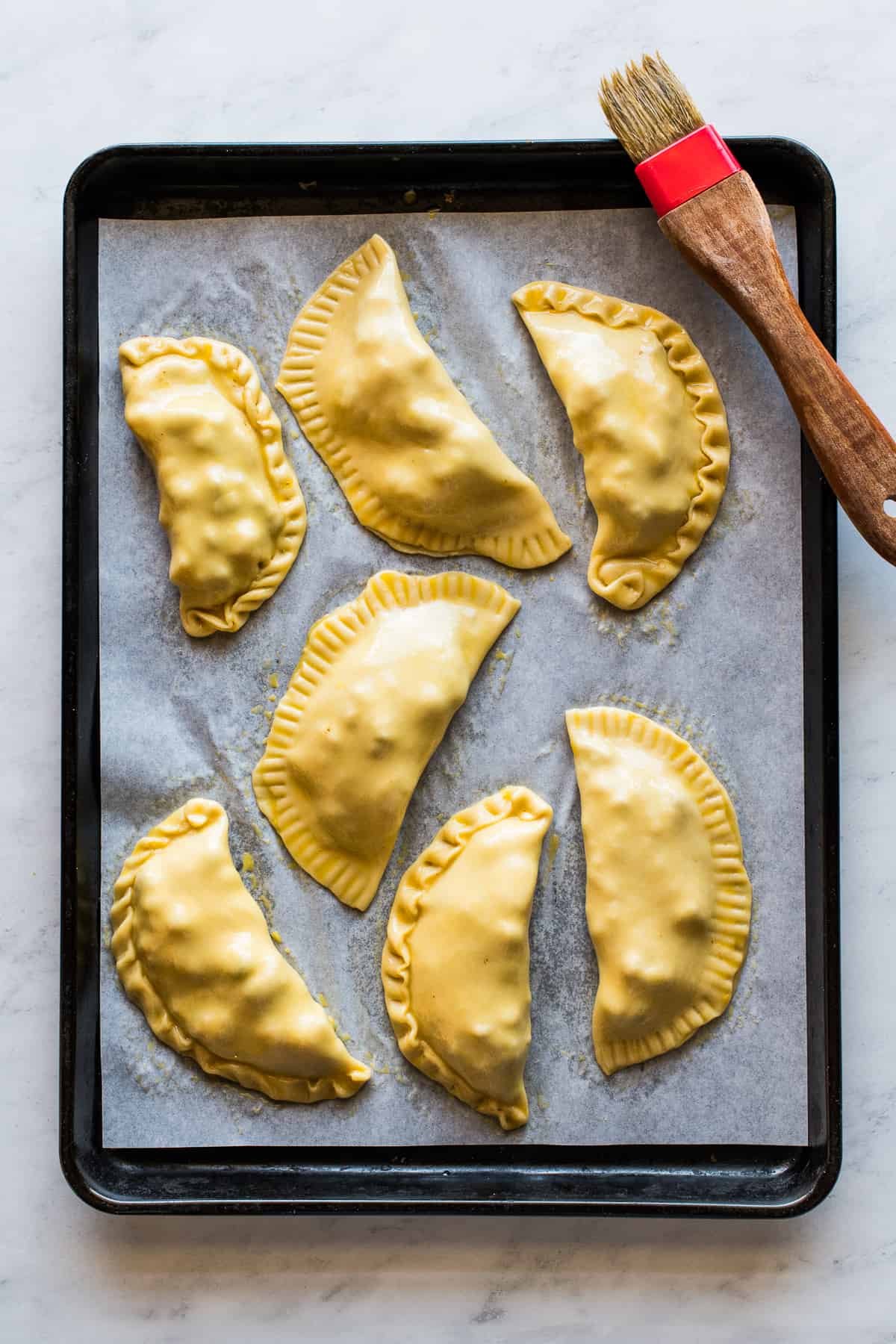 Empanadas sealed and brushed with an egg wash on a sheet pan ready to be baked.