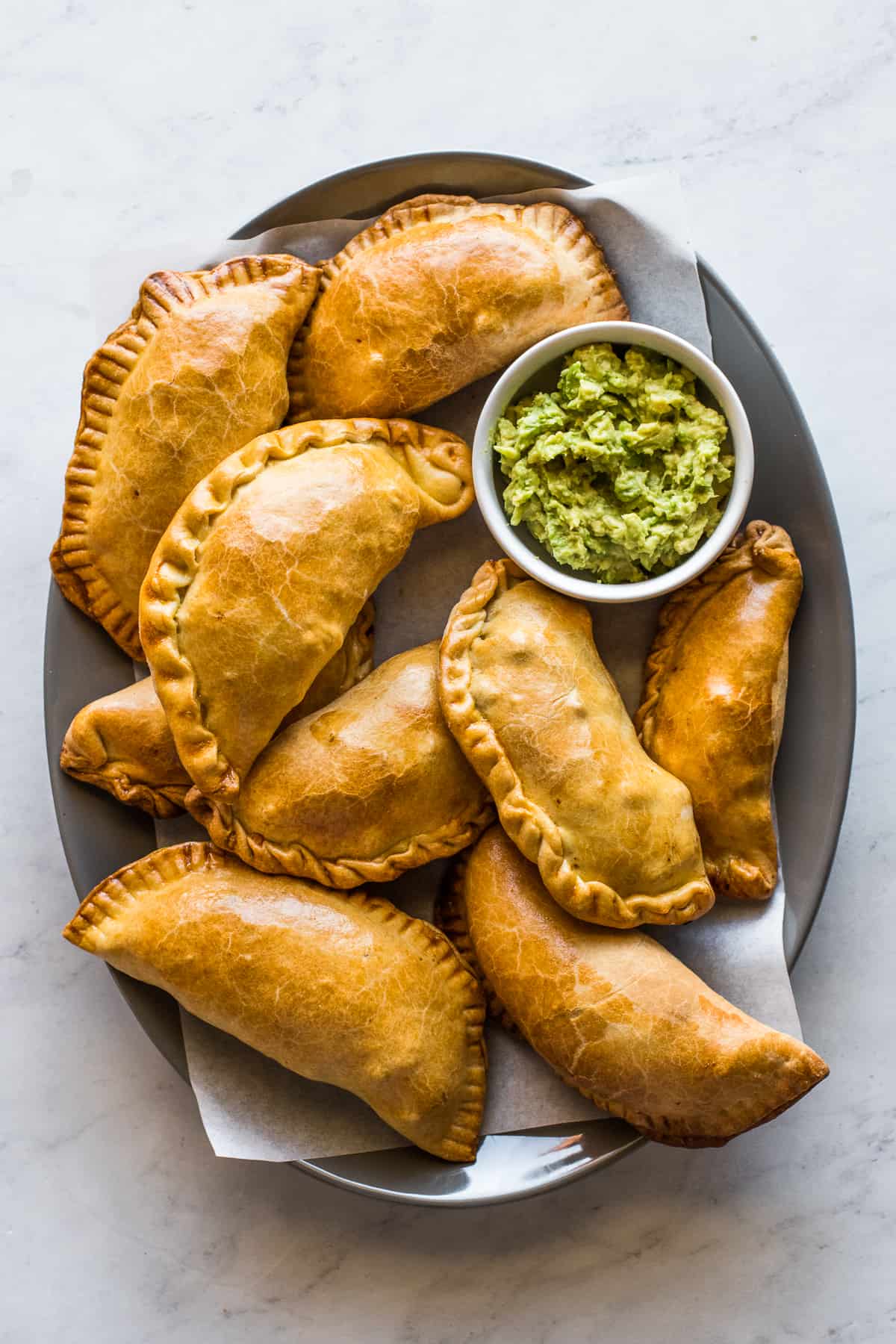 Beef empanadas on a platter with a bowl of guacamole on the side.