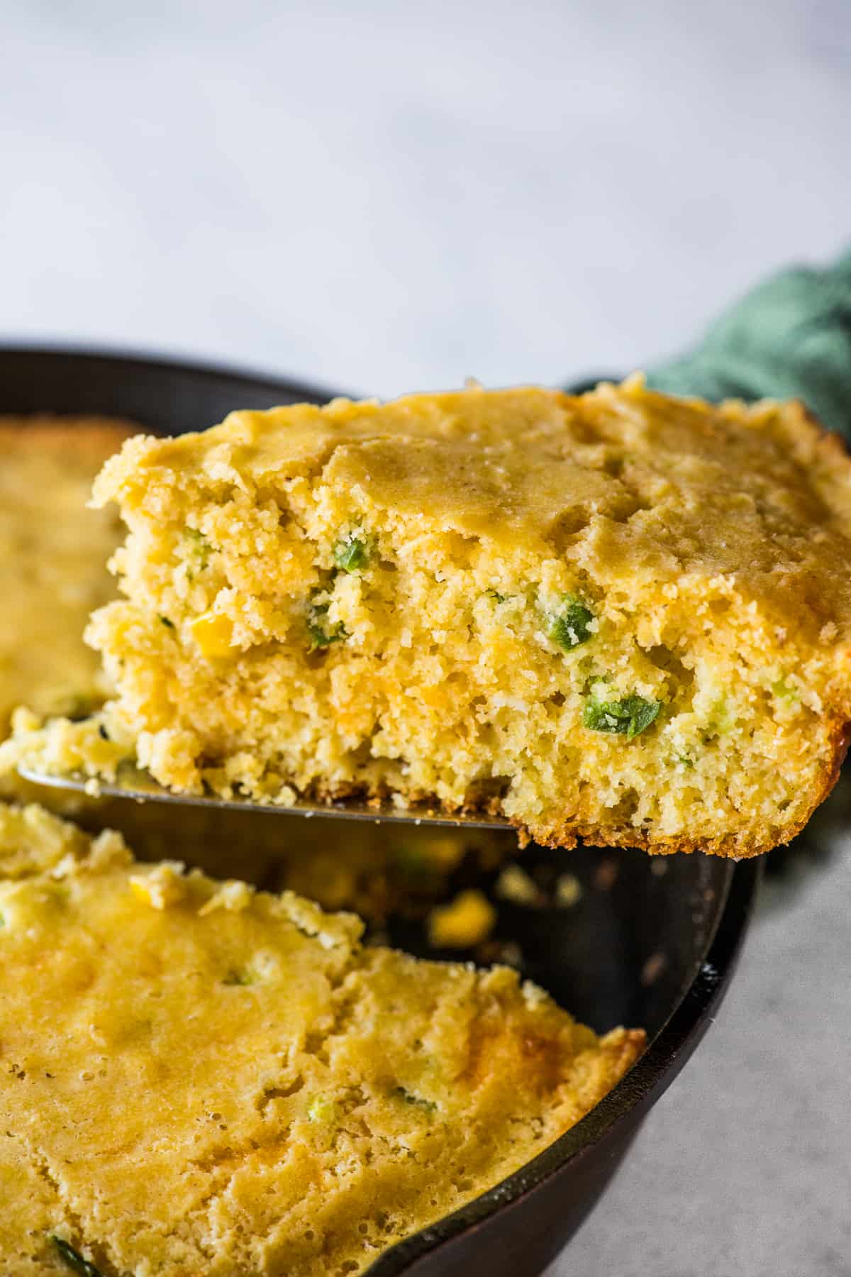 A slice of crumbly jalapeño cornbread with pieces of jalapeños and melted cheddar cheese.
