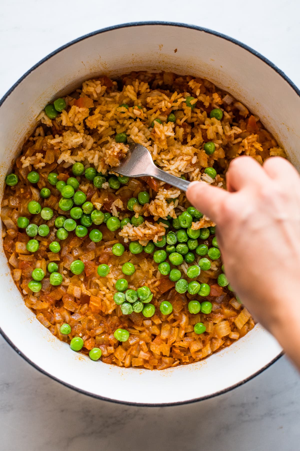 Authentic Mexican rice being fluffed with a fork with green peas on top.