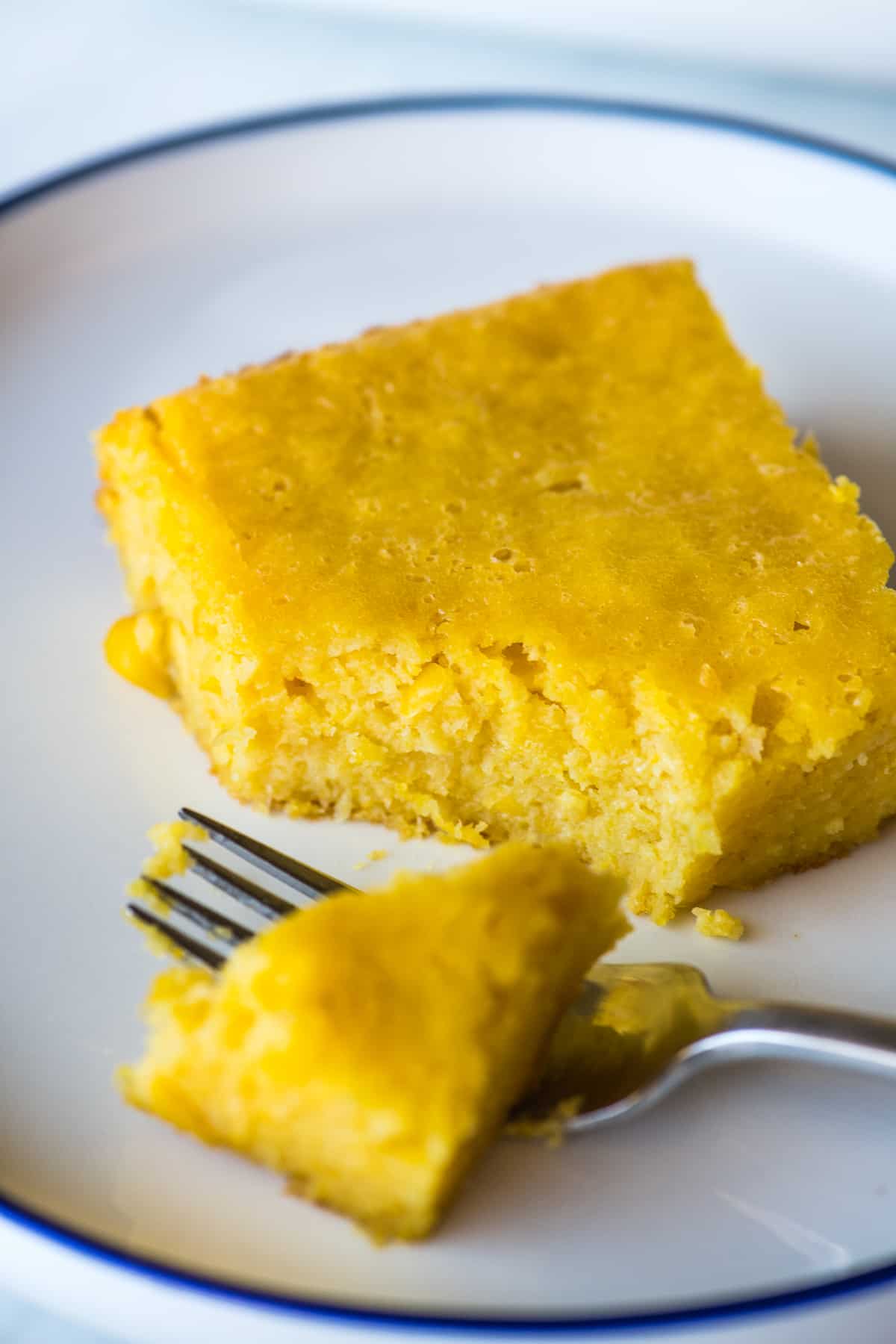 A slice of pan de elote on a plate with a portion of it on a fork ready to eat.