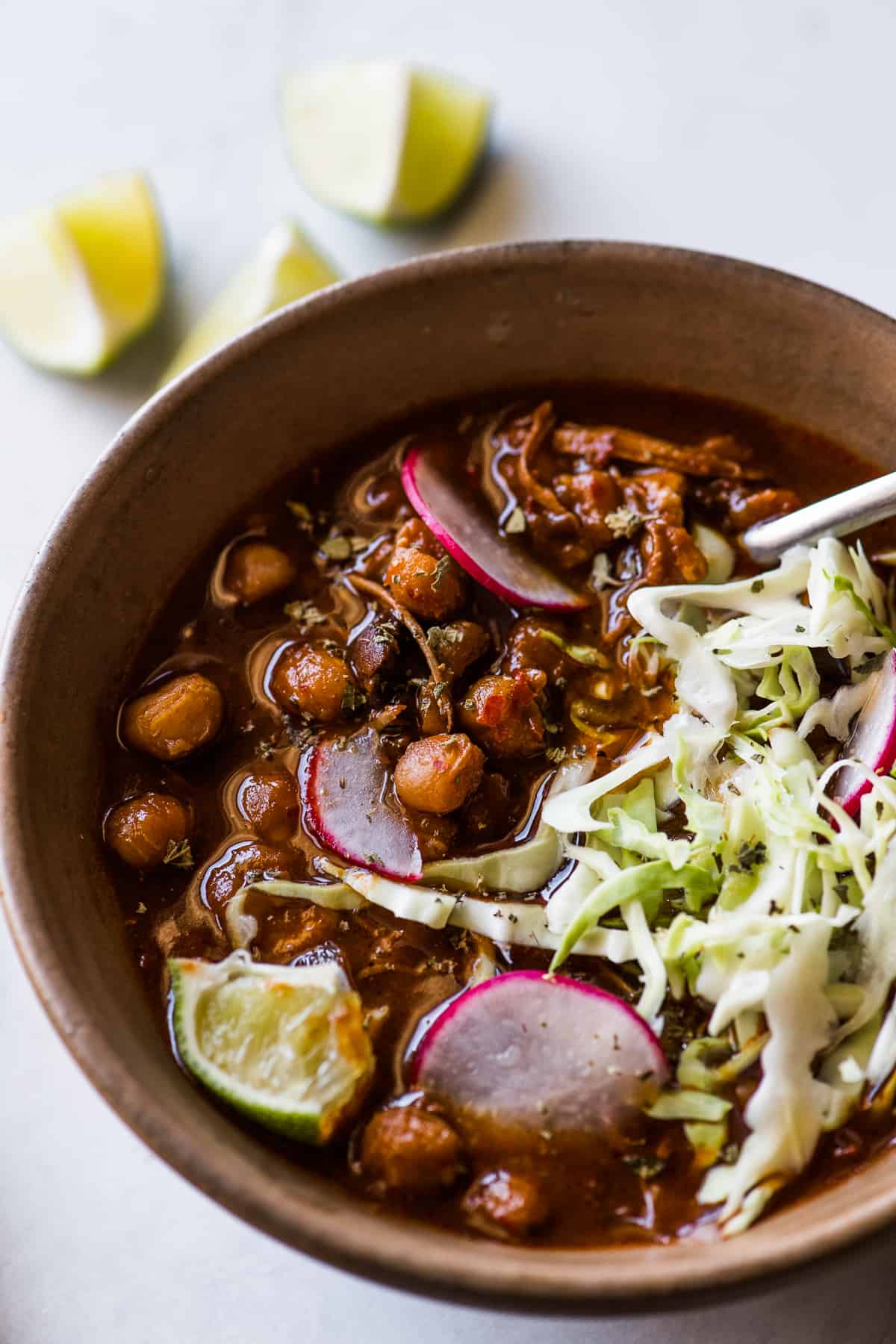 Pozole in a bowl topped with radishes, cabbage, Mexican oregano, and lime juice.