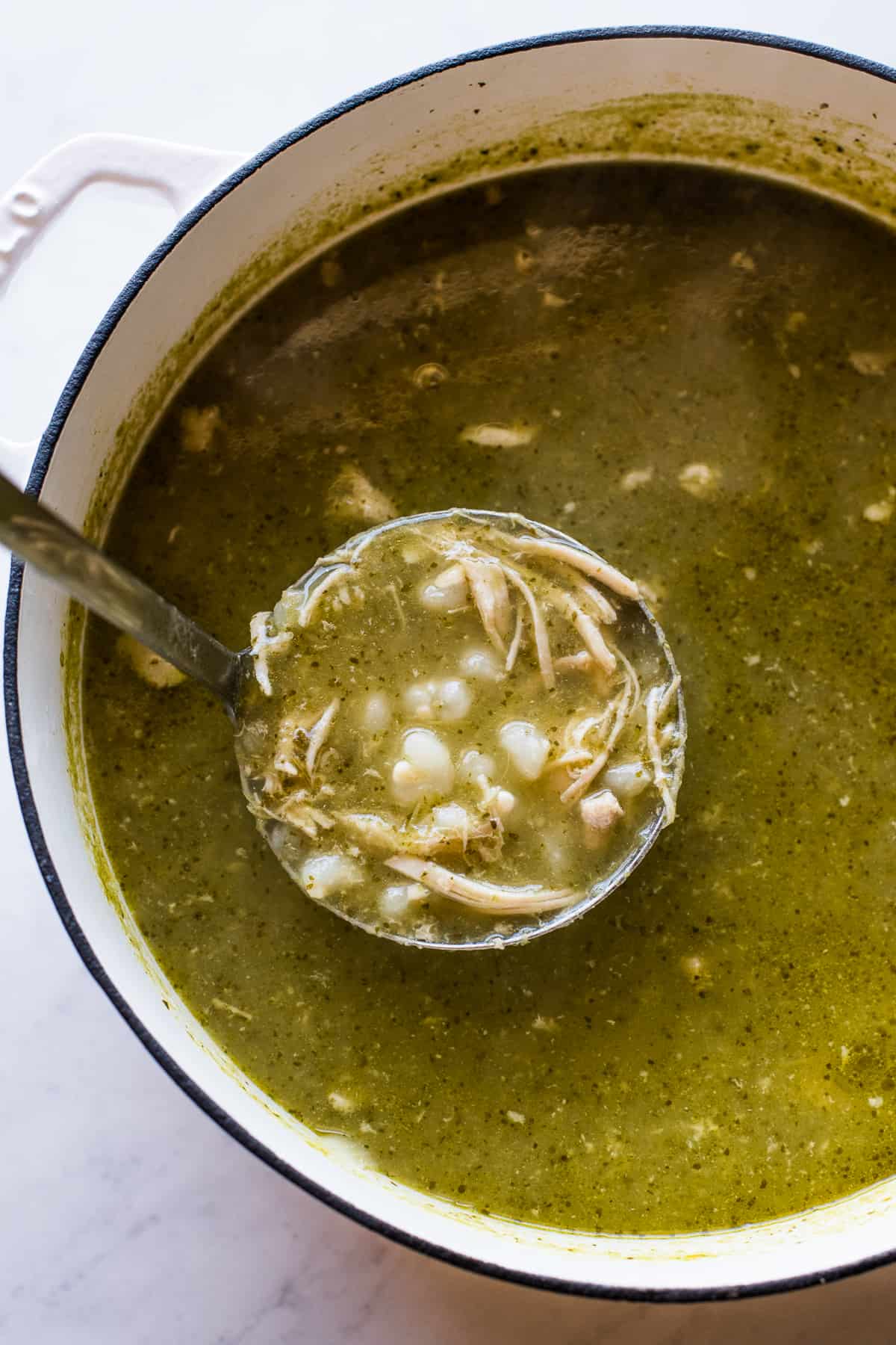 Pozole verde with chicken and hominy in a ladle about to be served.