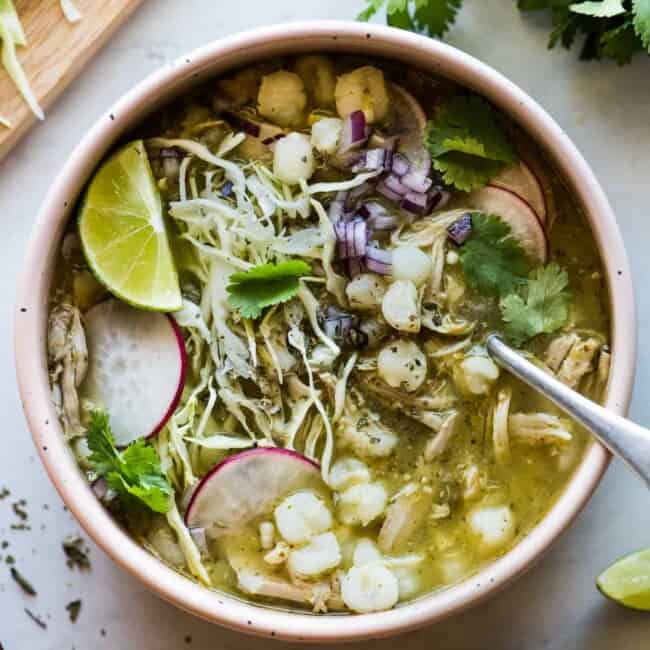 Pozole verde in a bowl topped with shredded cabbage, sliced radishes, cilantro, and lime juice.