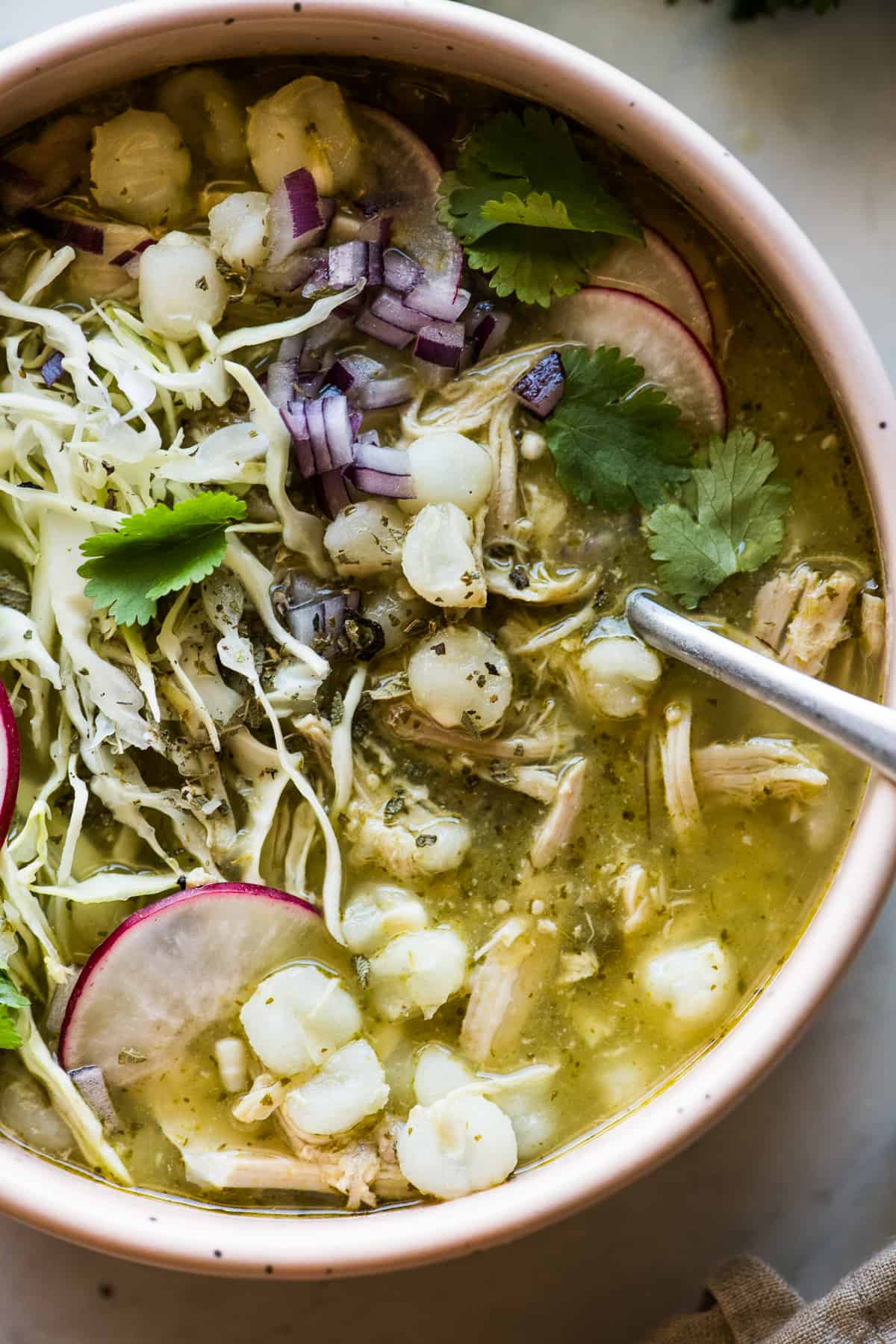 Chicken pozole verde (green pozole) in a bowl with a spoon ready to be eaten.