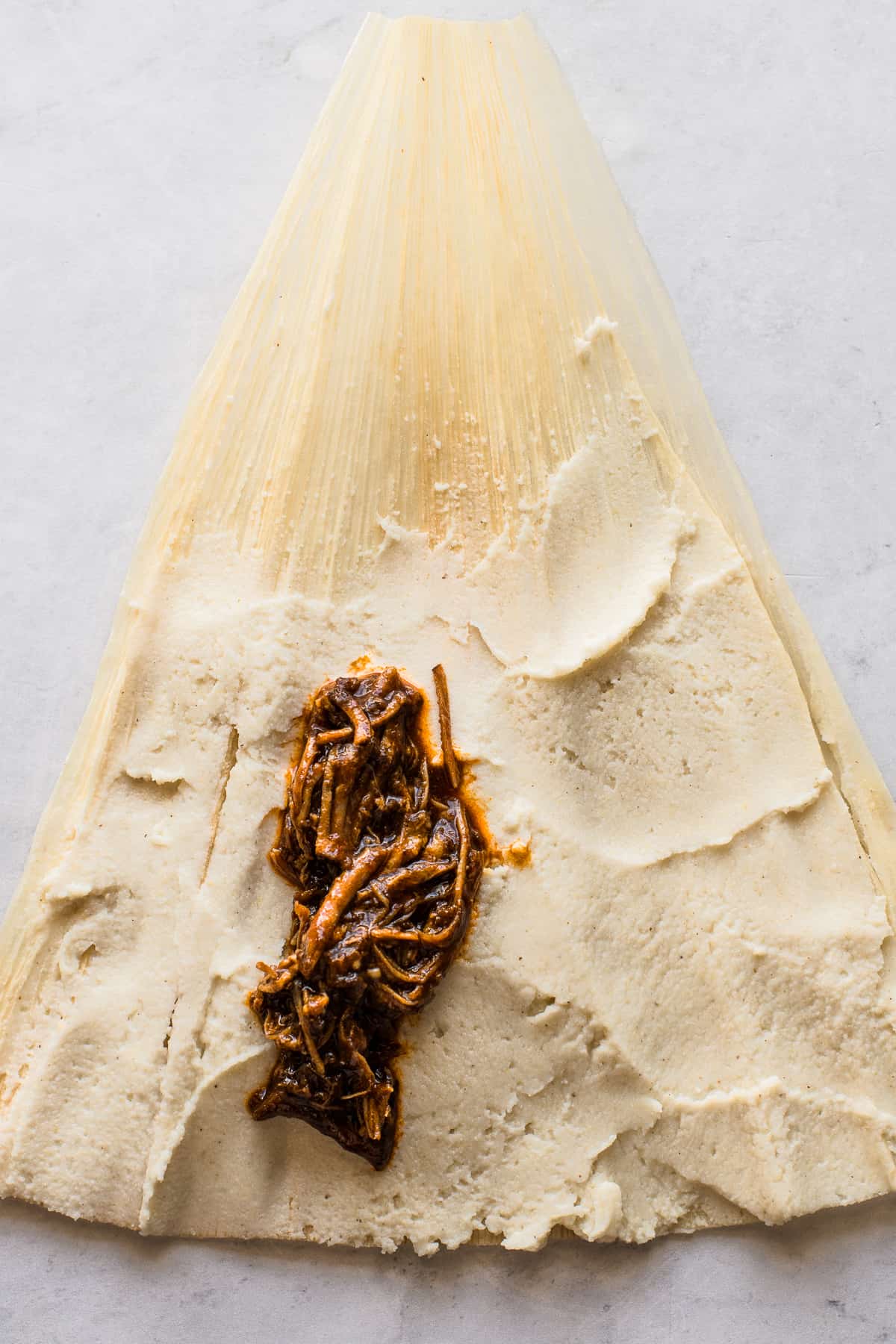 Shredded red chile pork on fresh masa dough on a corn husk.