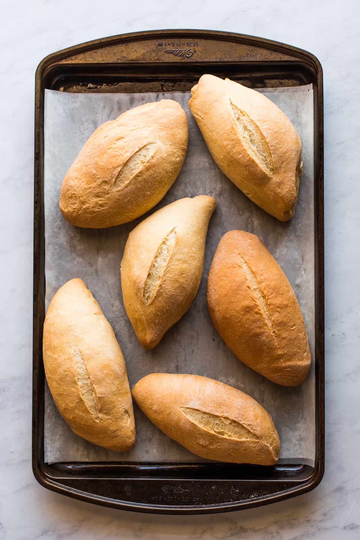 Six bolillo breads on a baking sheet ready to eat.