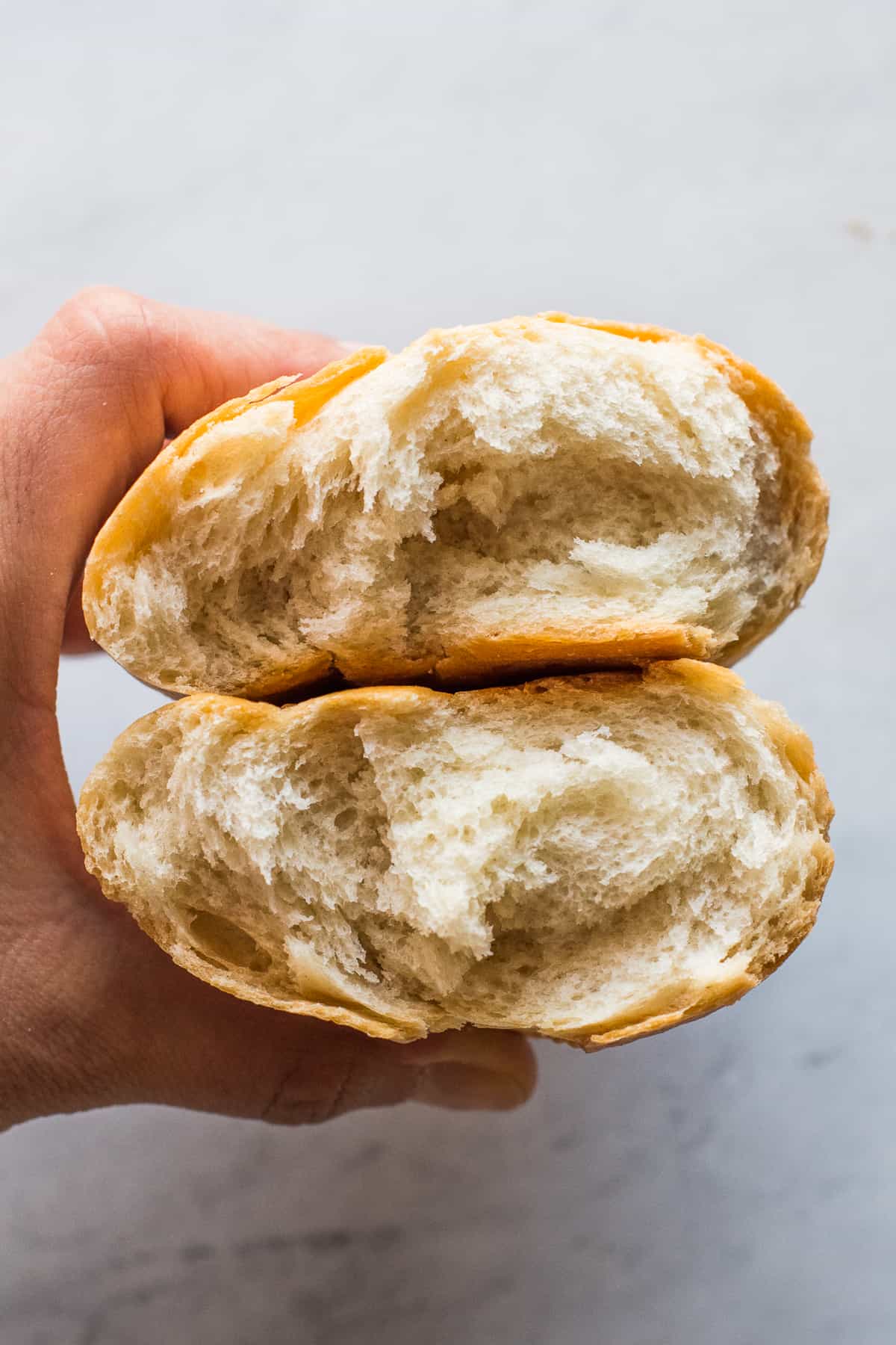 A bolillo bread cut in half to show the soft white bread inside in contrast to the crispy golden brown crust on the outside.