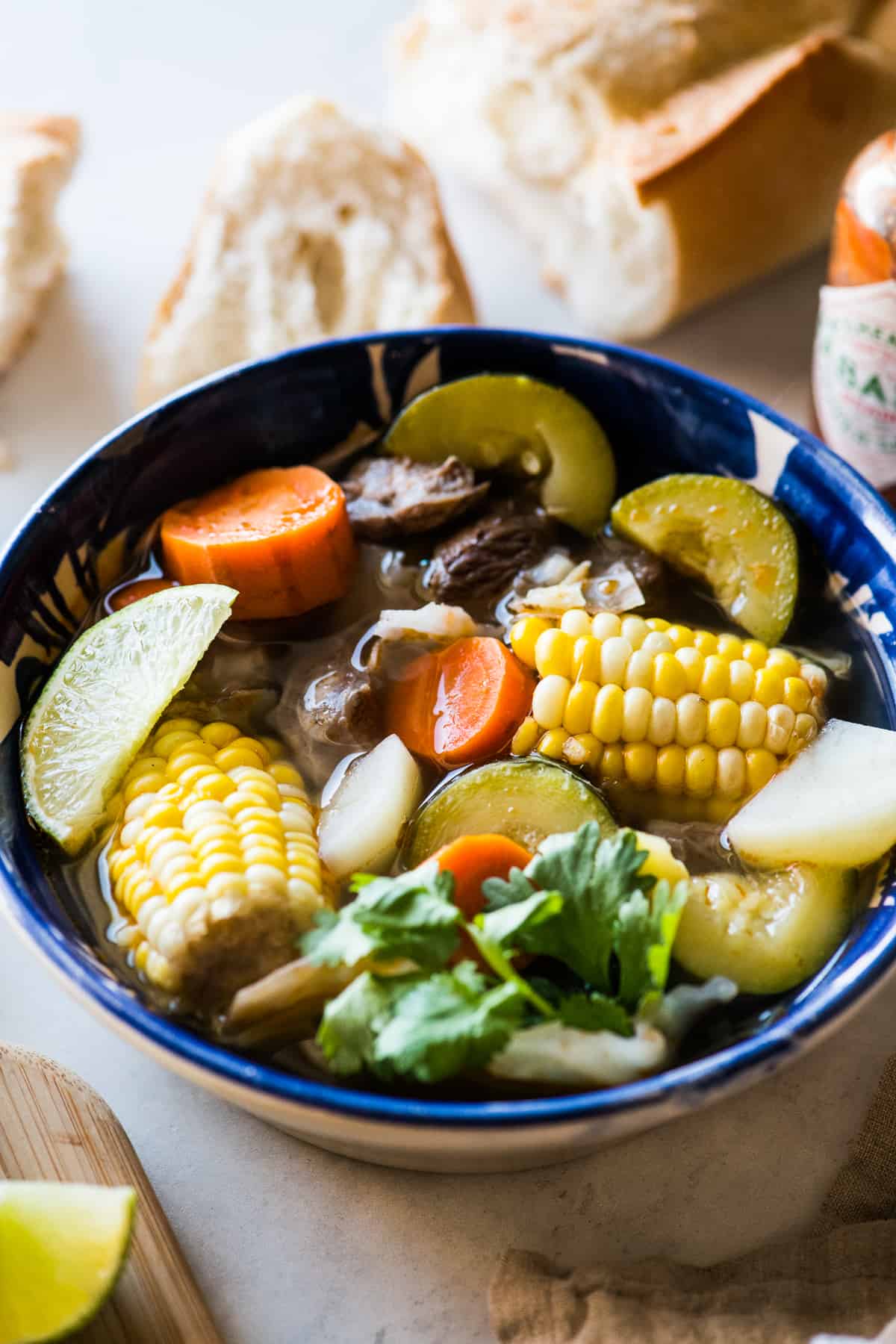 Caldo de Res in a bowl served with chunks of carrot, zucchini, potatoes, cilantro, and more.