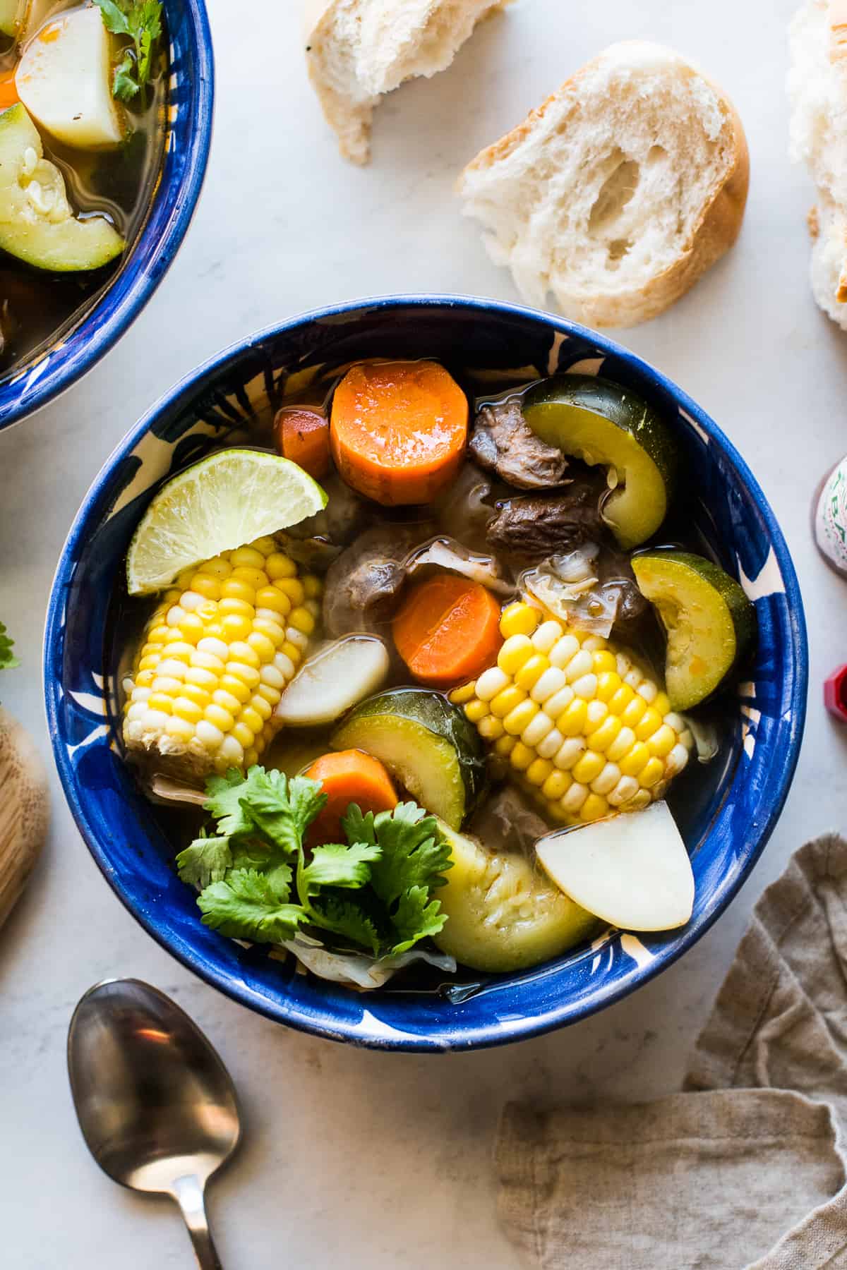 Caldo de Res in a bowl garnished with cilantro and a lime wedge.