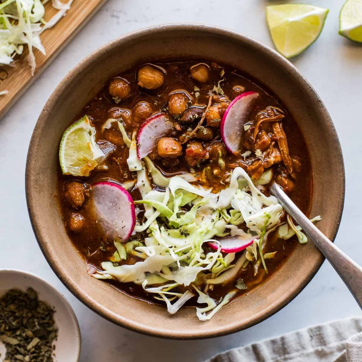 Pozole Rojo in a bowl topped with shredded cabbage, sliced radishes, and a lime wedge.