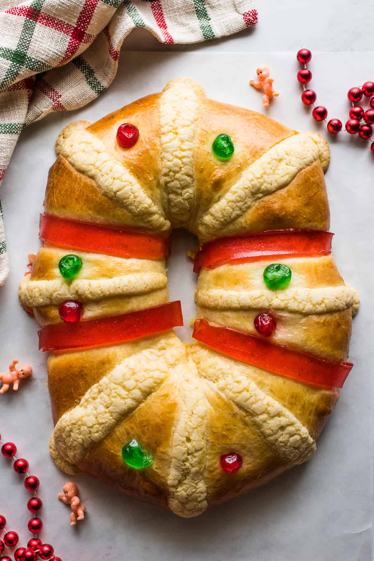 Rosca de Reyes decorated with candied cherries, guava paste and baby Jesus figurines on a table.