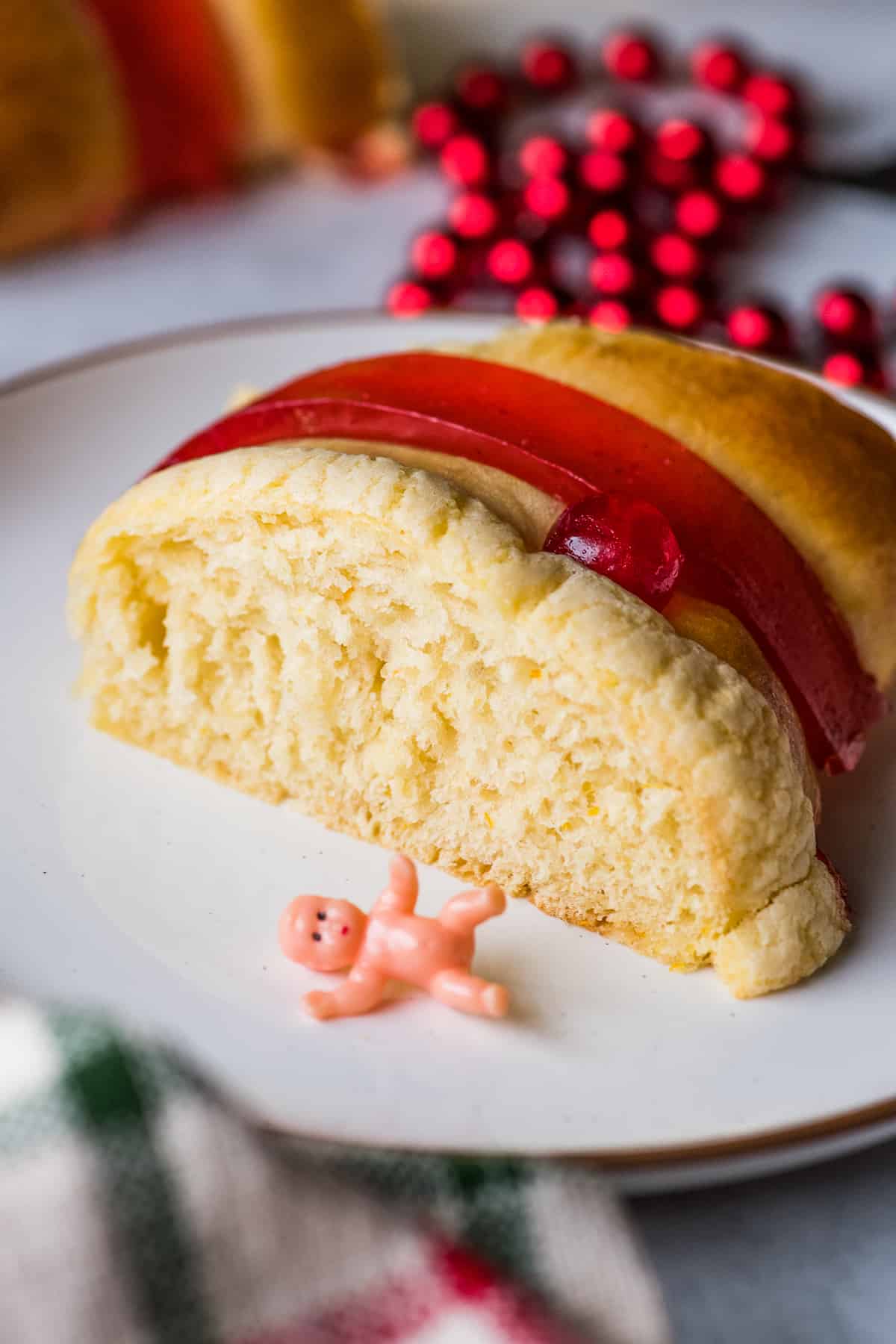 A slice of Rosca de Reyes bread on a plate with a baby Jesus figurine next to it.