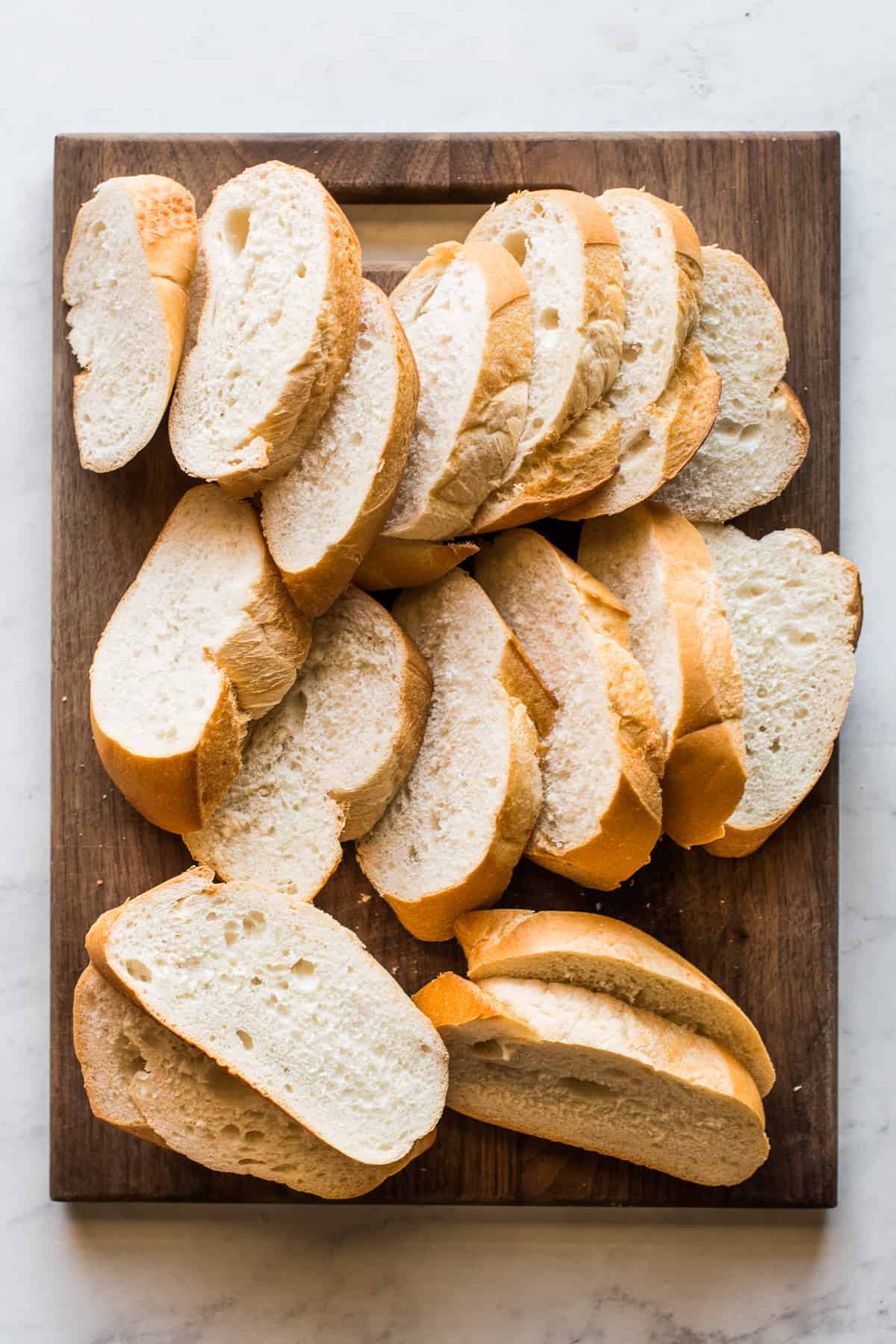 Slices of bolillo bread on a cutting board for torrejas.
