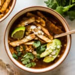 Chicken tortilla soup in a bowl topped with tortilla strips, cilantro, avocado, and queso fresco.