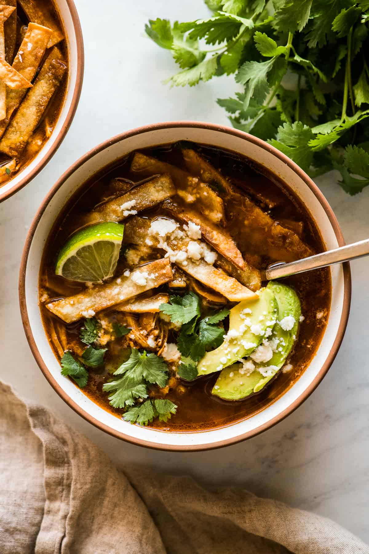 Chicken tortilla soup in a bowl topped with tortilla strips, cilantro, avocado, and queso fresco.