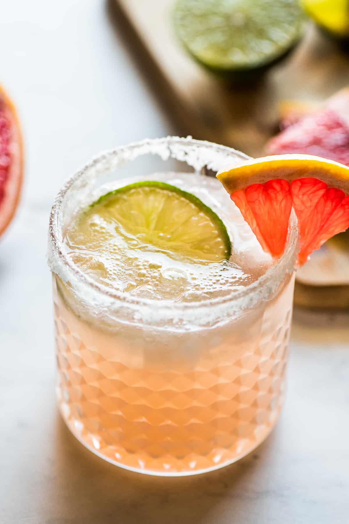 A paloma recipe drink in a glass with a salted rim and garnished with lime and grapefruit.